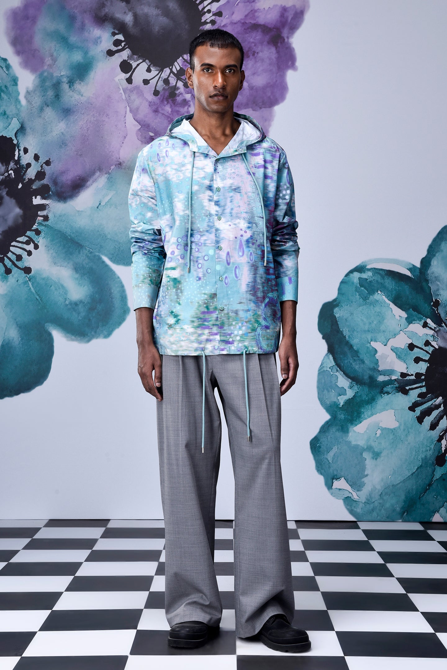 Male model wearing artistic print hoodie shirt by Stylera in pastel blue floral print with gray wide leg trousers