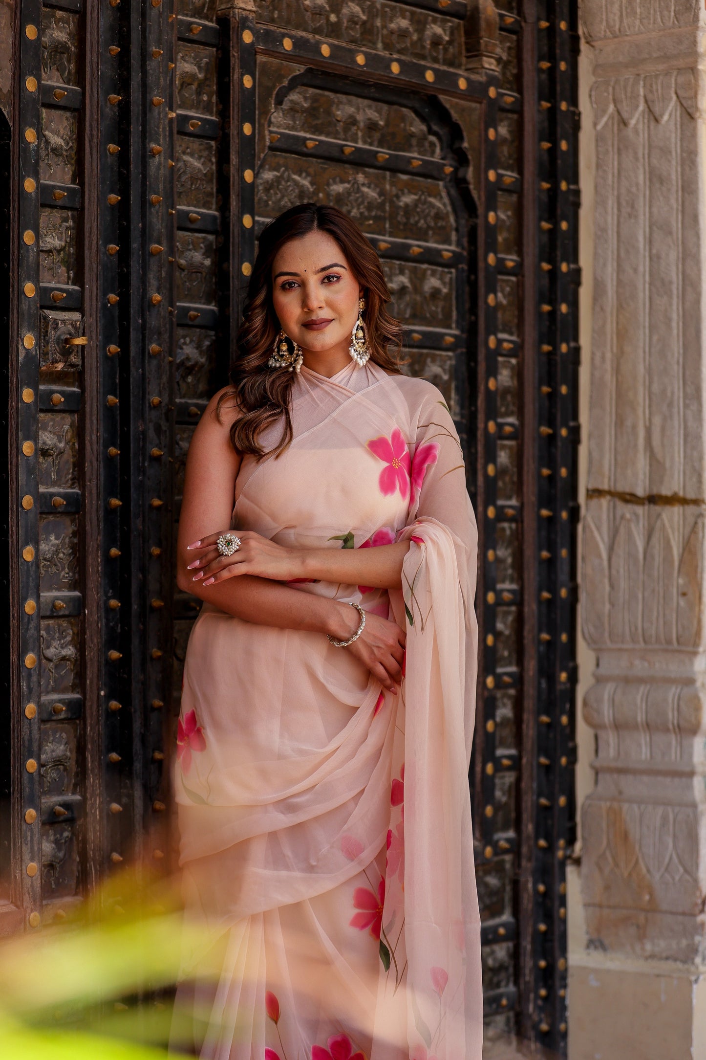 Elegant woman in a beige floral chiffon saree with pink flowers, styled gracefully for festive occasions.