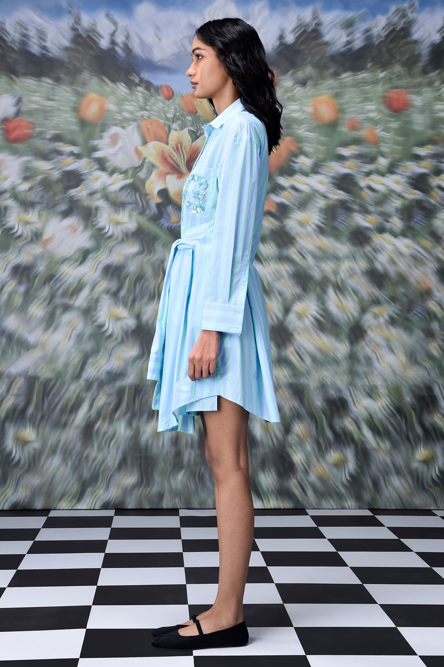 Stylera model in blue green stripe dress shirt style belted mini dress side profile with floral backdrop