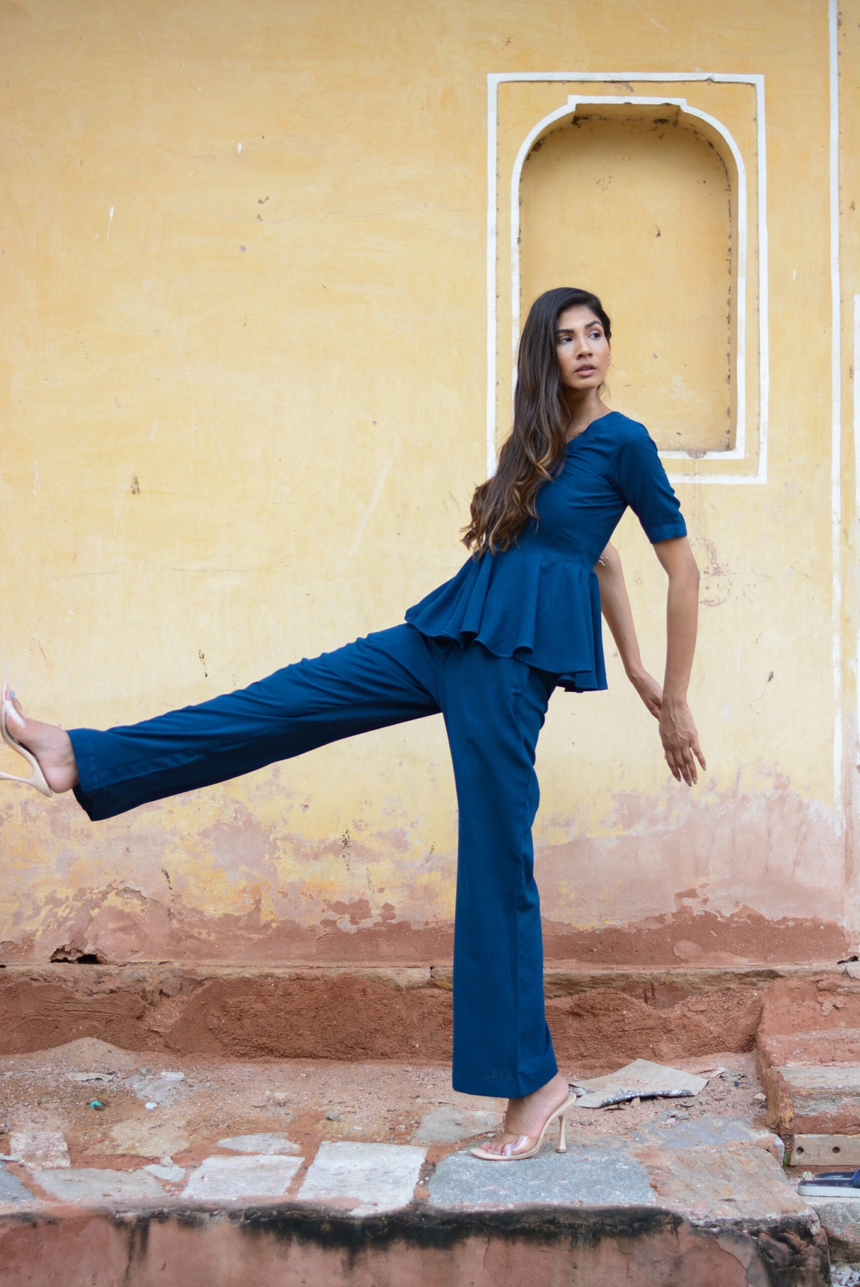 Yale blue peplum co-ord set displayed by model against a rustic yellow wall