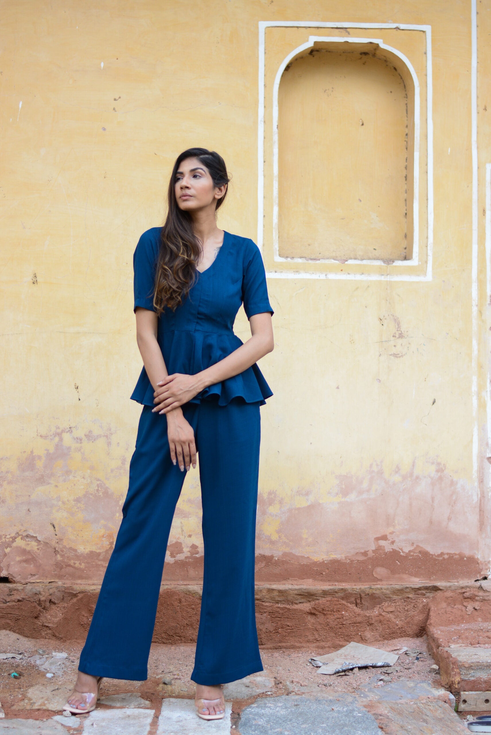 Model wearing a Yale blue peplum co-ord set standing against a textured yellow wall