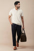 Casual linen polo for men in cream with a relaxed fit, paired with checked pants and a stylish bag.