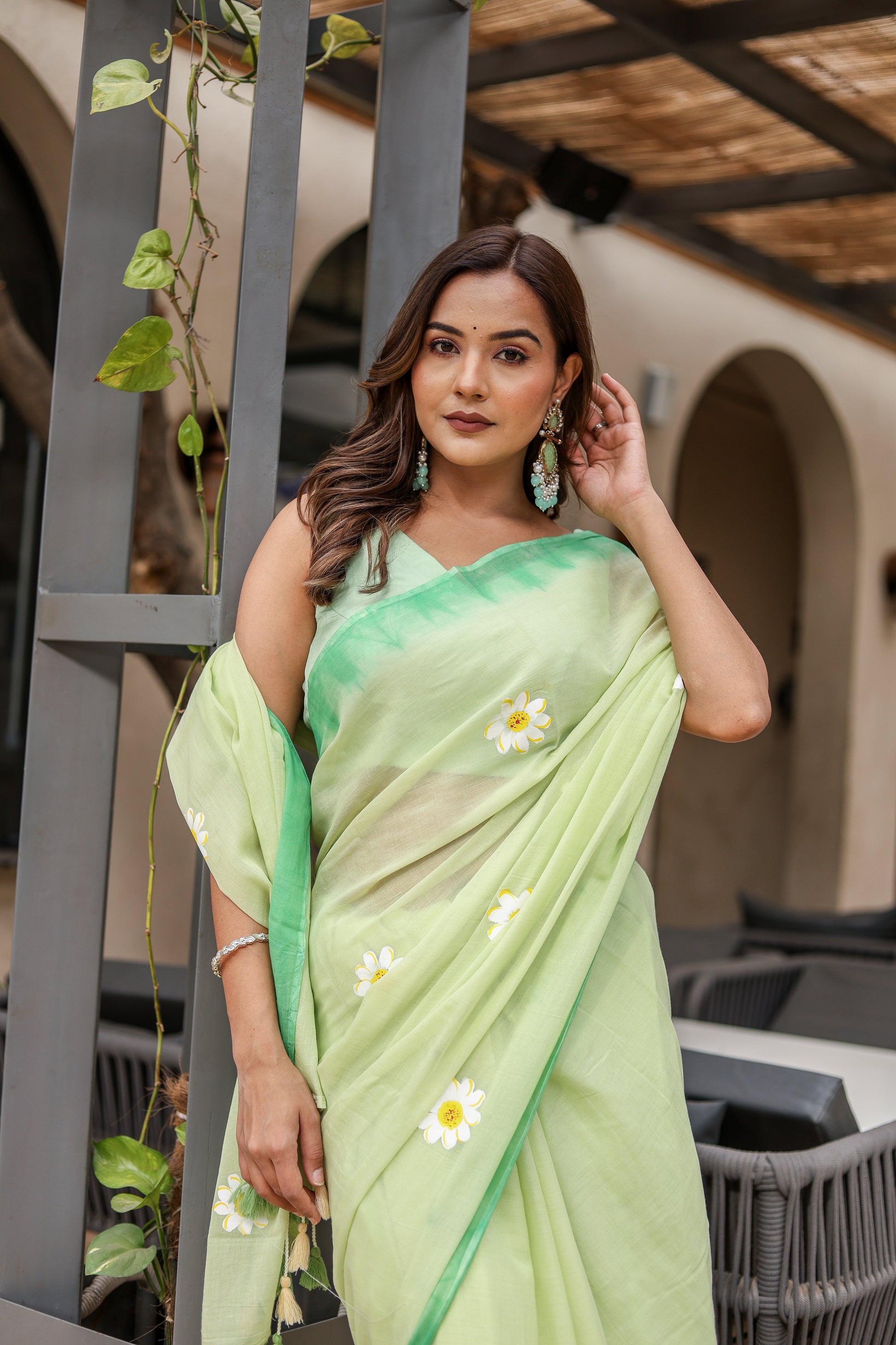 Elegant designer malmal saree with flowers in soft green color, worn by a woman with matching earrings