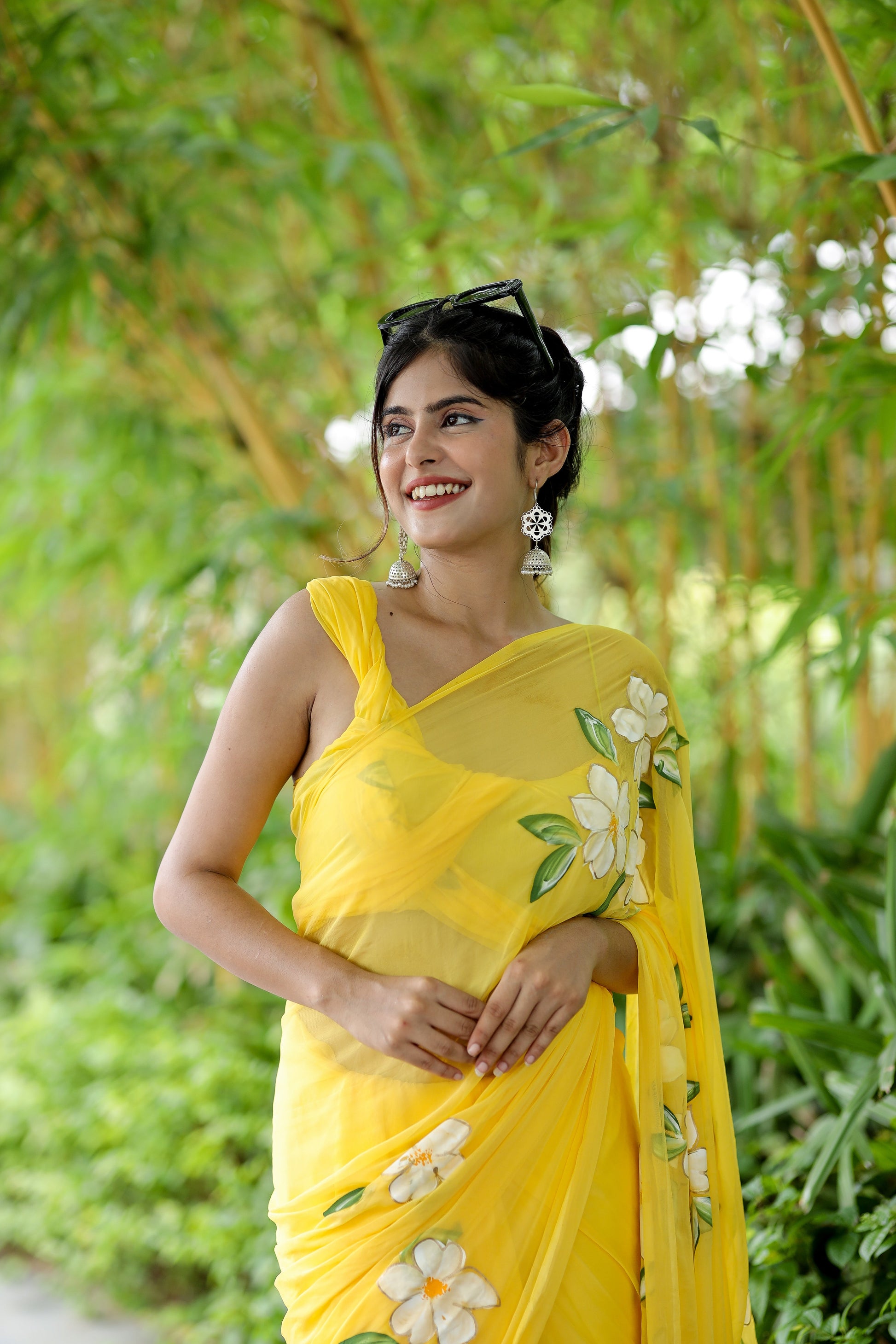 Bright yellow designer saree with floral art displayed by a smiling woman outdoors