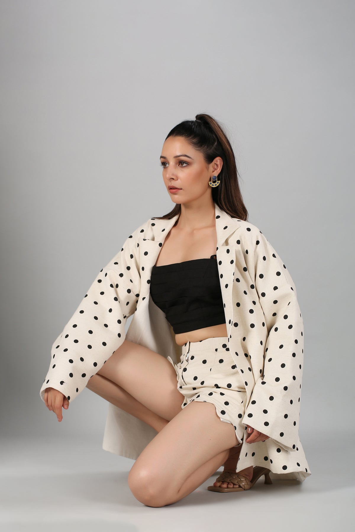 Model wearing Stylera polka dot blazer and shorts with black crop top kneeling in fashionable two piece suit for ladies