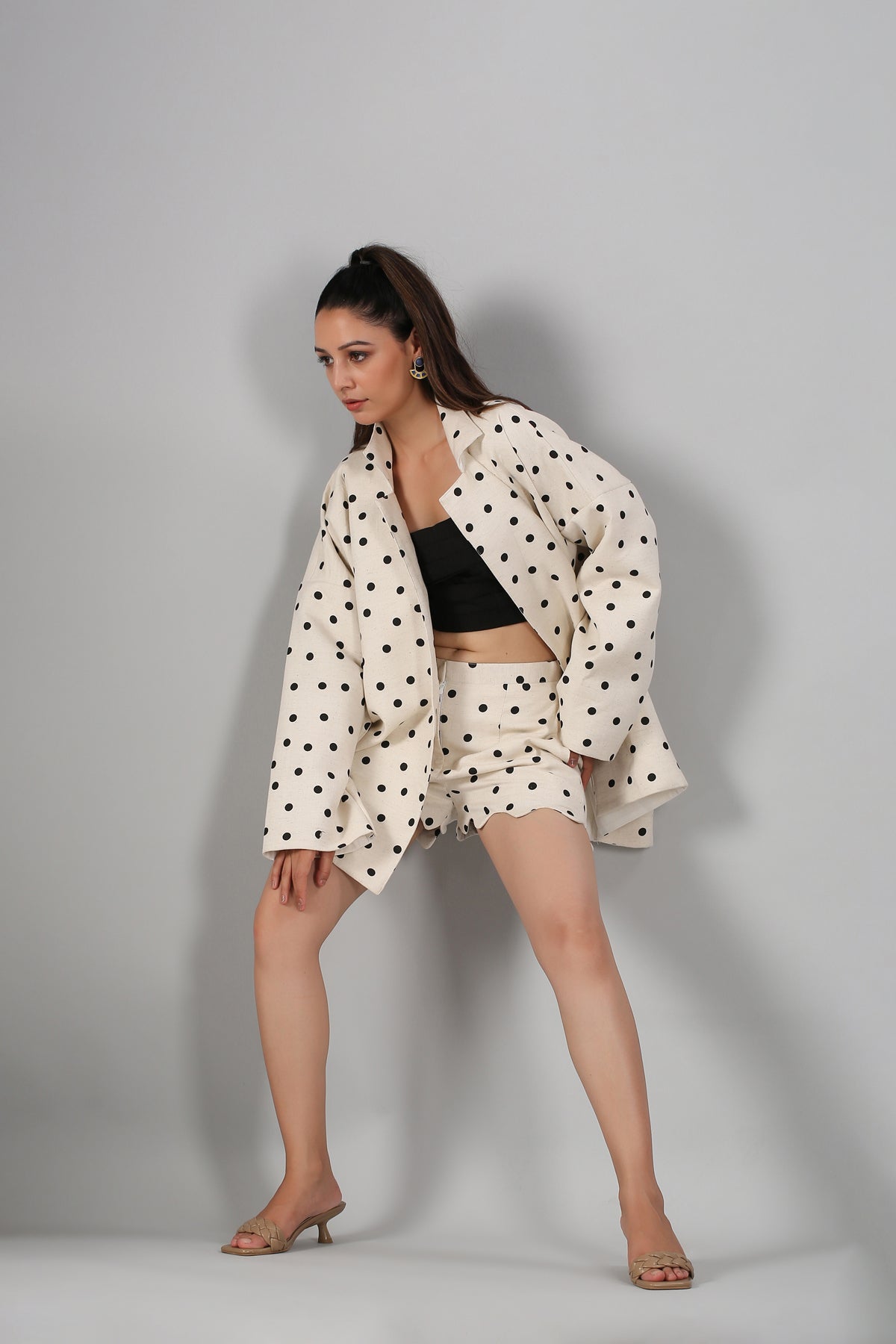Woman wearing Stylera fashionable two piece suit for ladies cream polka dot jacket and matching shorts with black crop top and heels