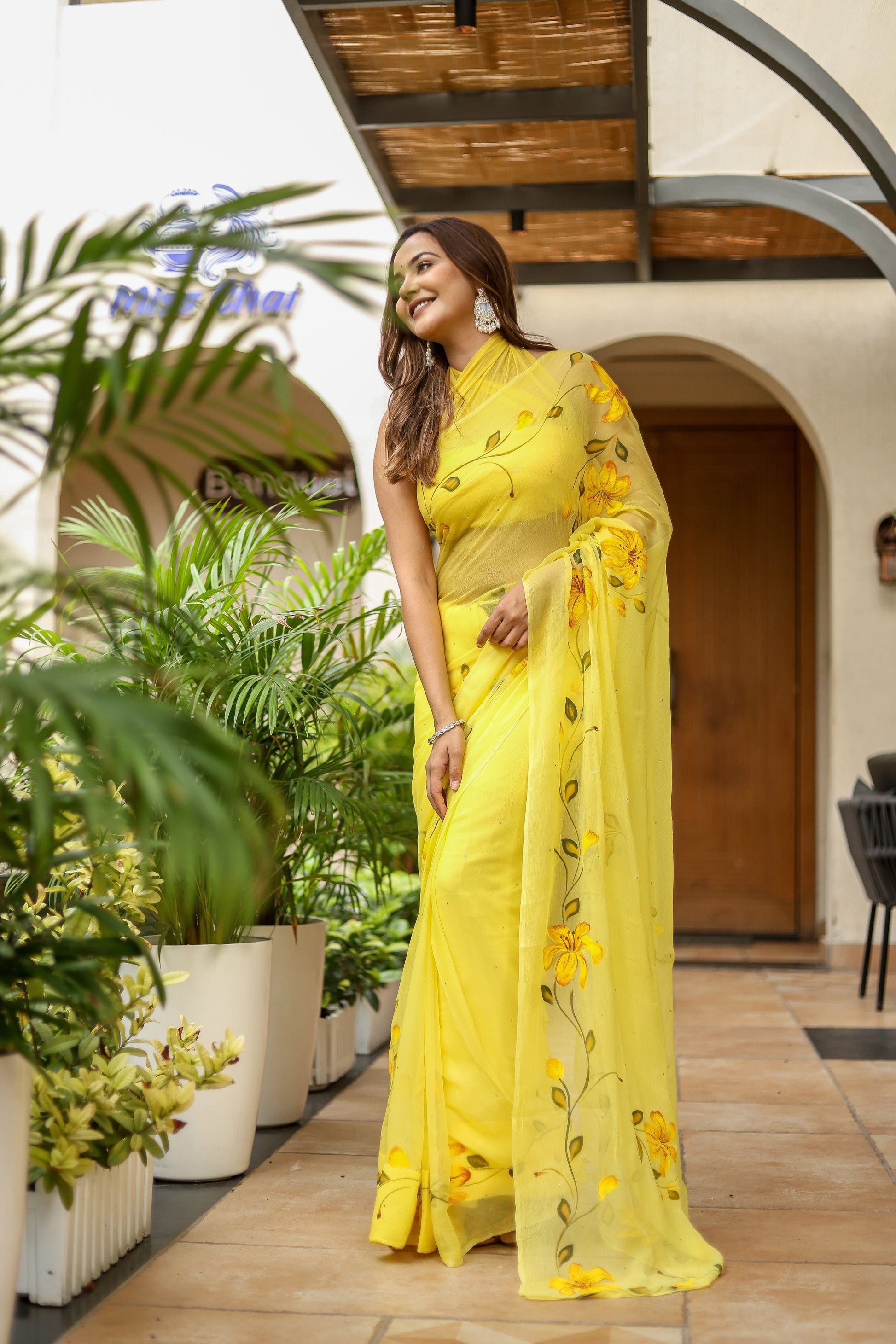 Stylish woman wearing a floral viscose chiffon saree with mukaish work in yellow, standing outdoors
