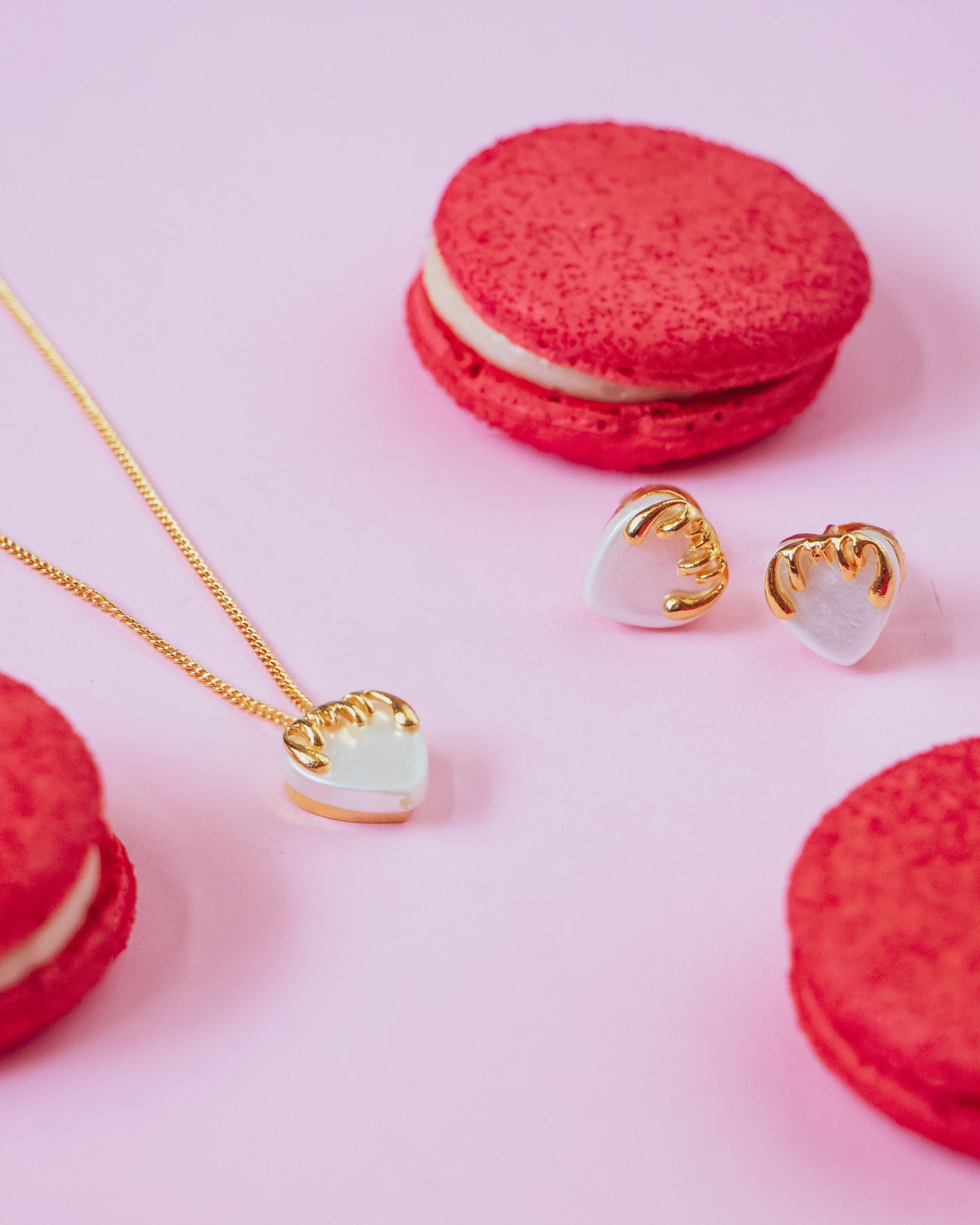 Stylera gold heart necklace for women displayed with matching heart earrings and red macarons