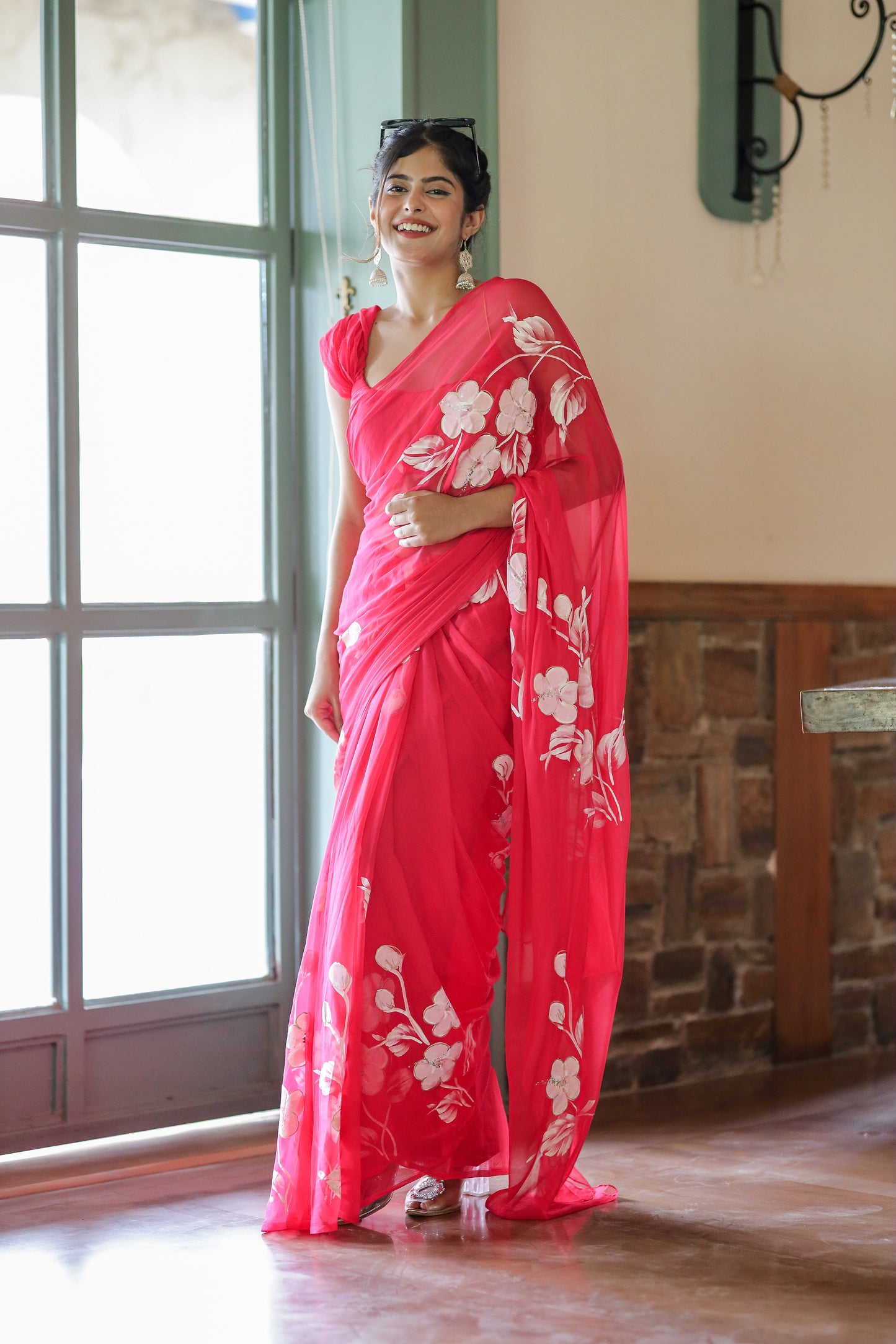 Woman wearing a handpainted chiffon saree rani pink with floral designs, styled elegantly indoors