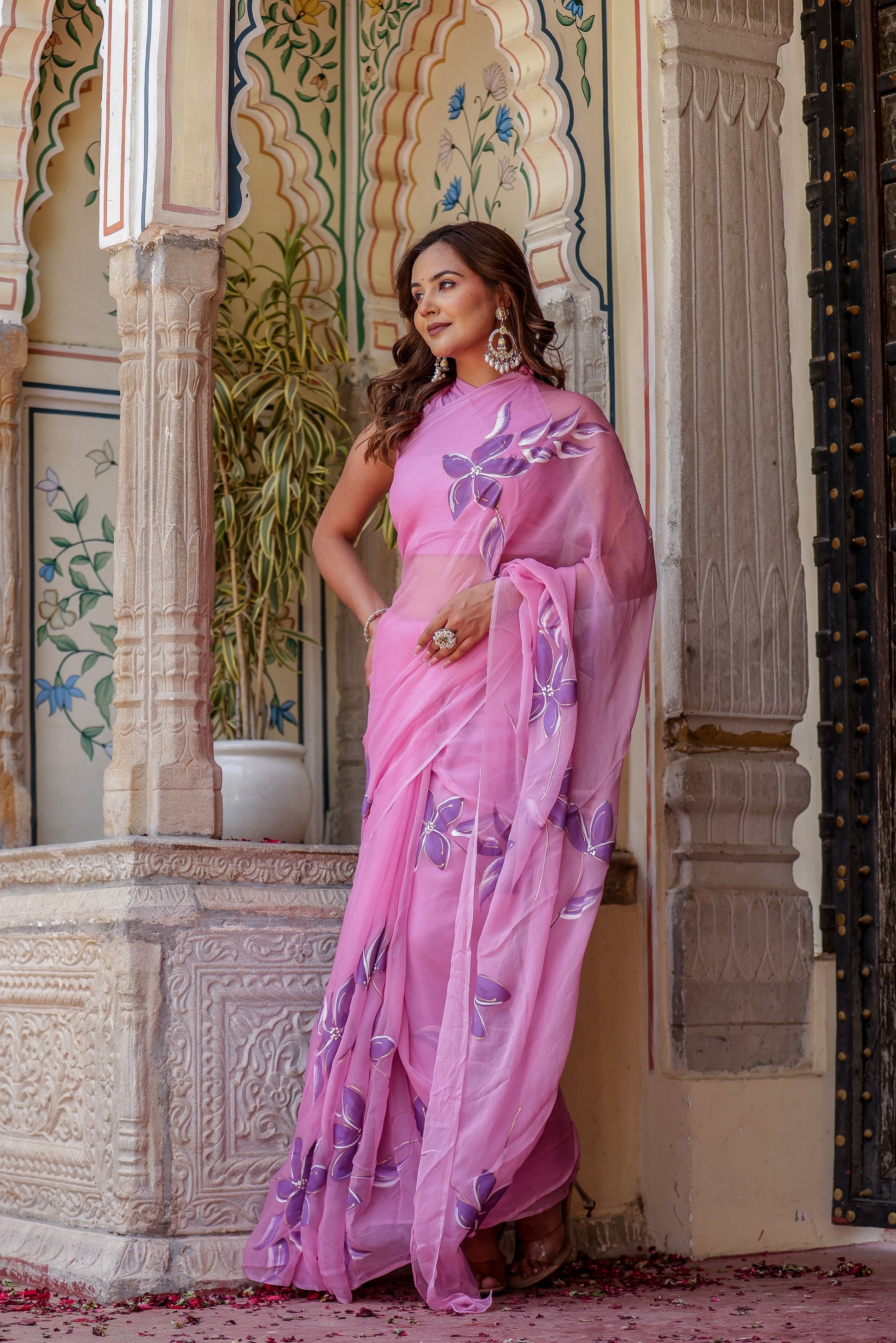 Elegant model wearing a handpainted lavender chiffon saree with intricate floral designs in a picturesque setting