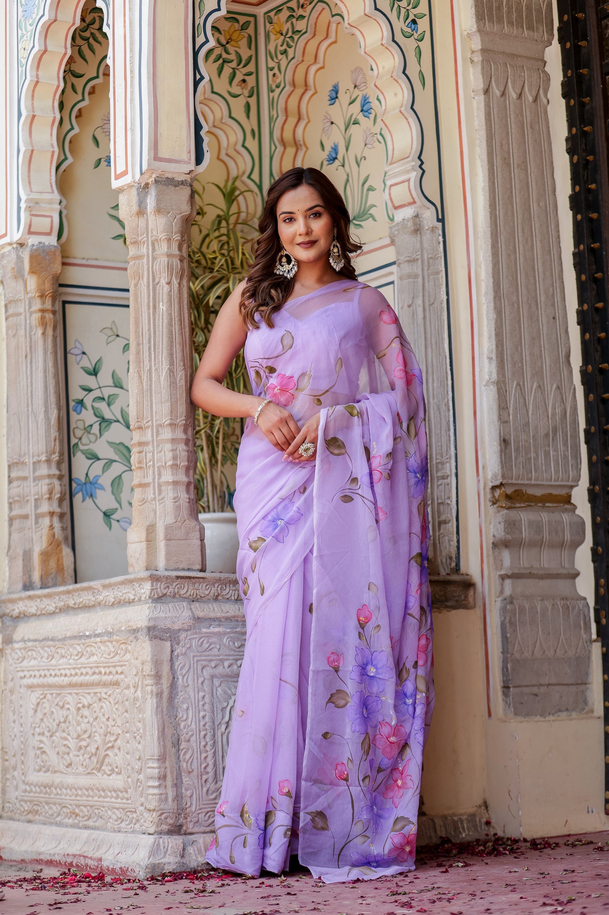 Elegant woman wearing a handpainted lavender chiffon saree with floral designs in a historic setting