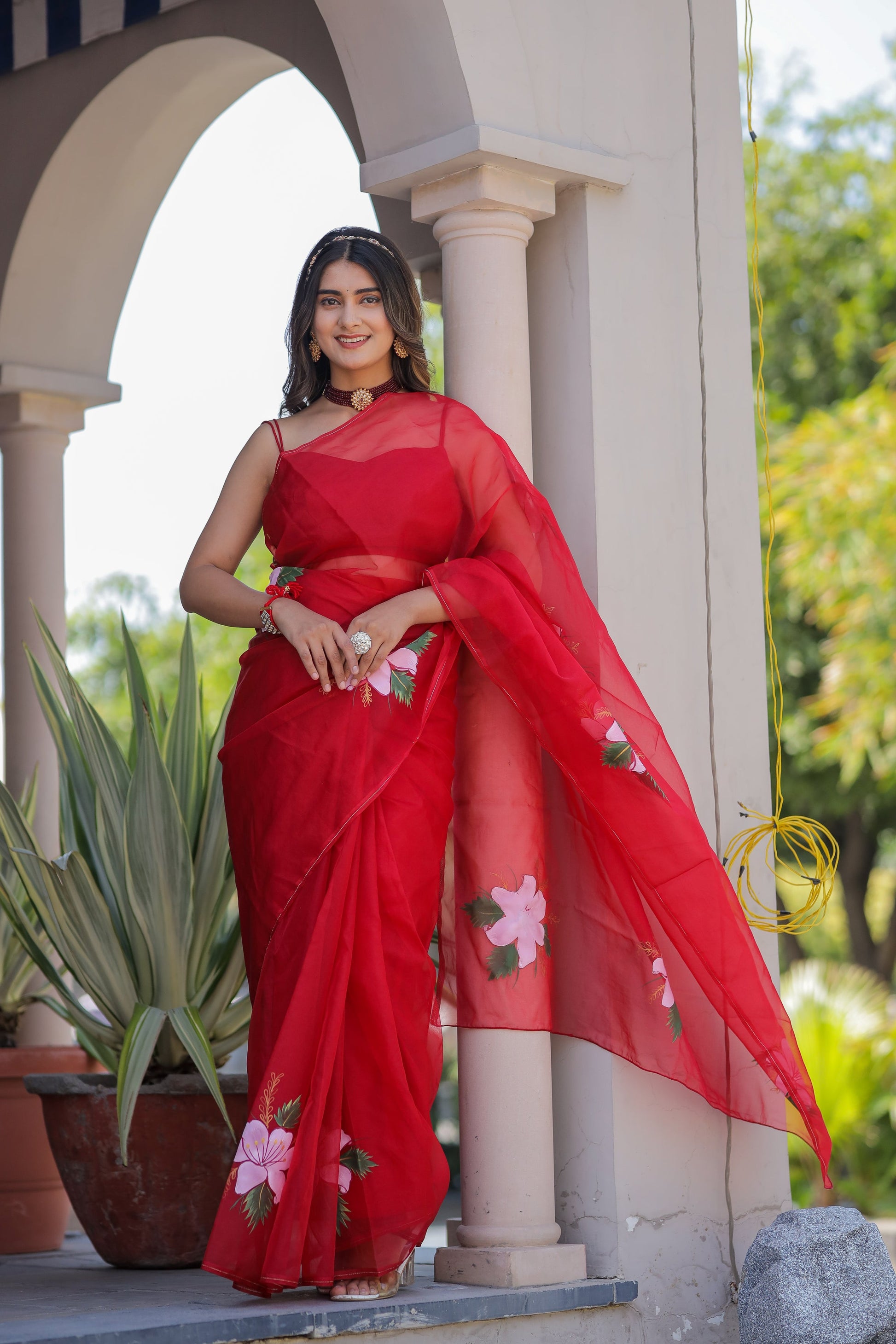 Elegant woman wearing a handpainted red organza saree with floral designs, perfect for festive occasions