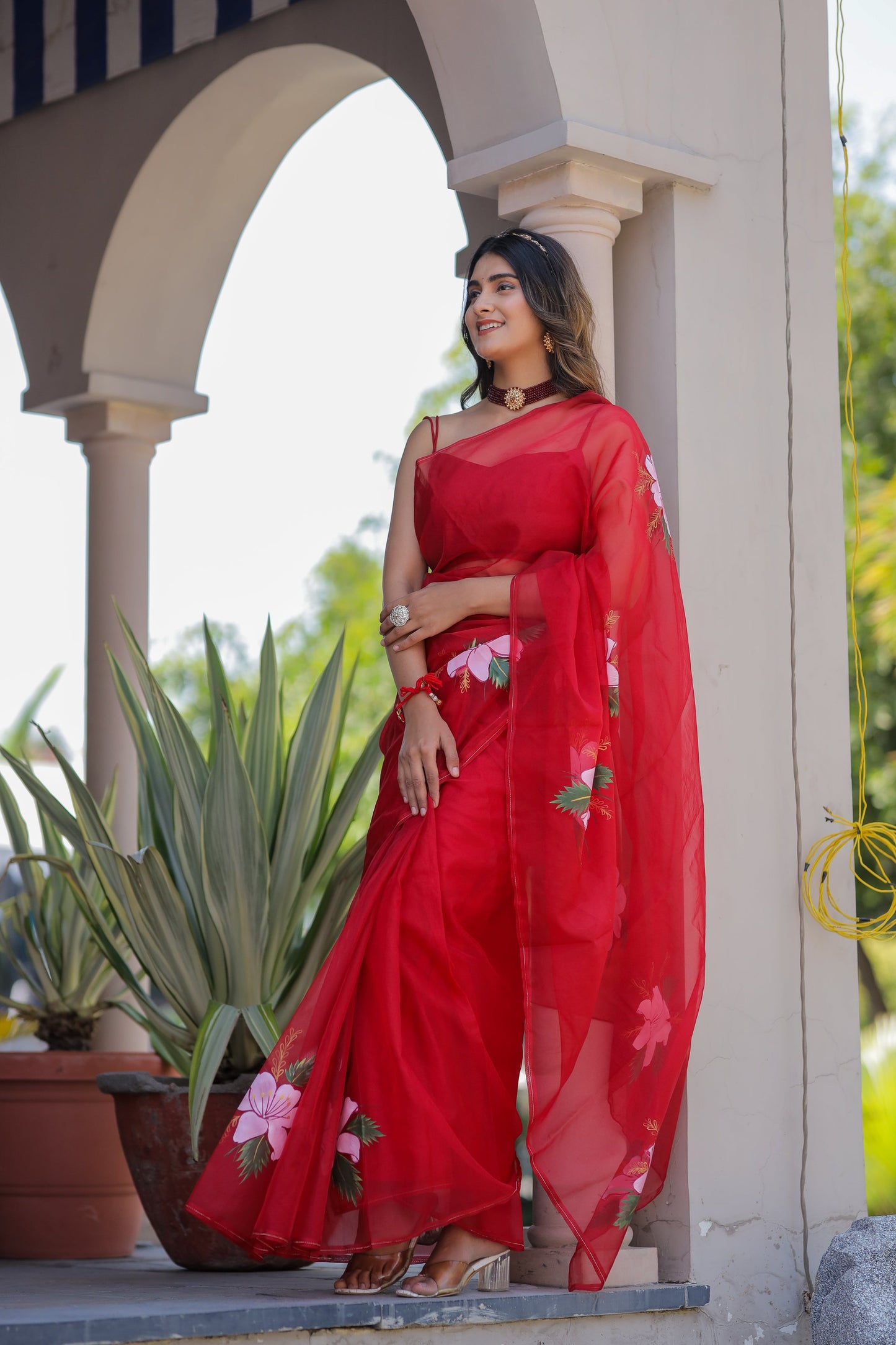 Elegant woman wearing a handpainted red organza saree with floral designs, styled with matching accessories