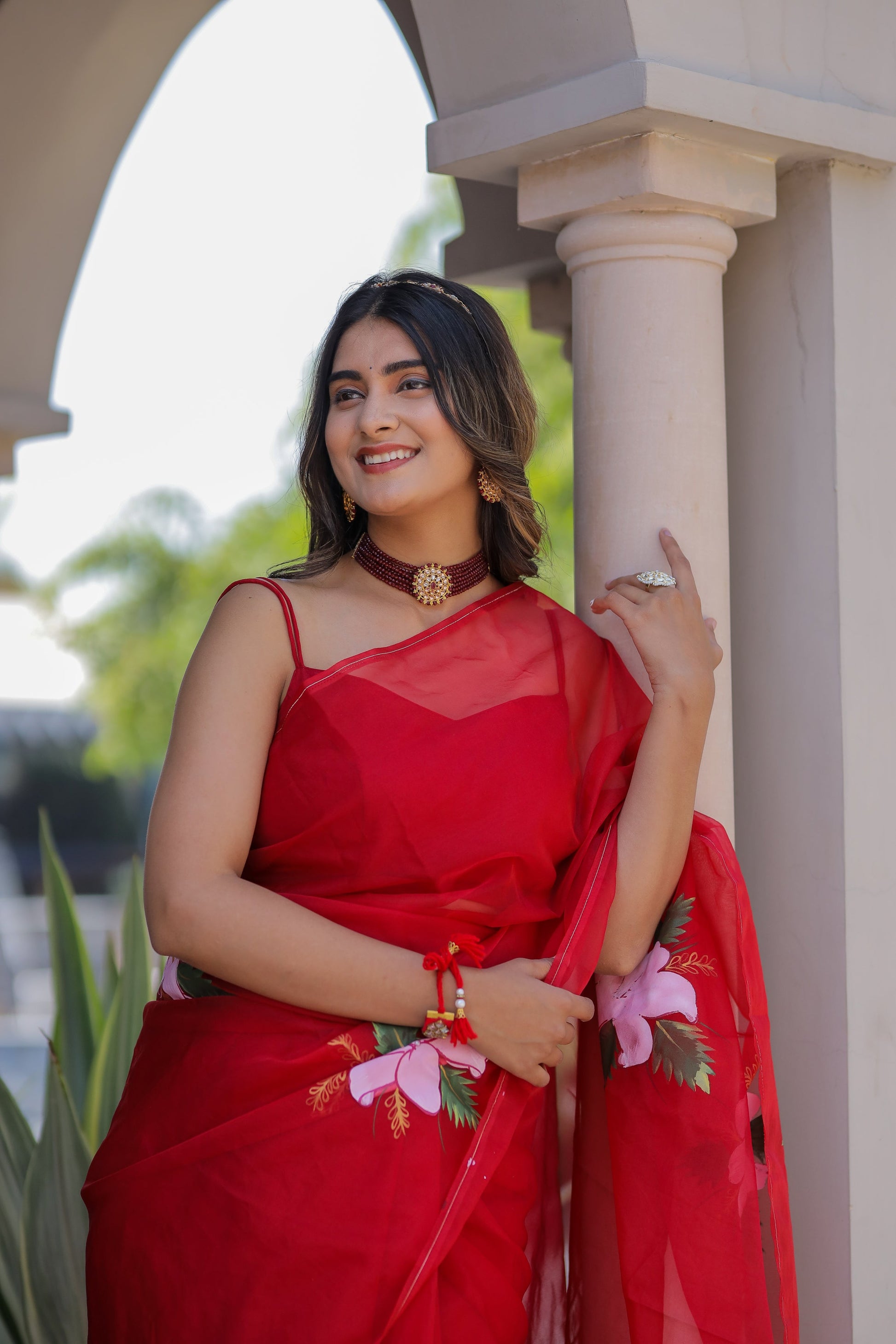 Model wearing a handpainted red organza saree with floral designs, perfect for festive occasions