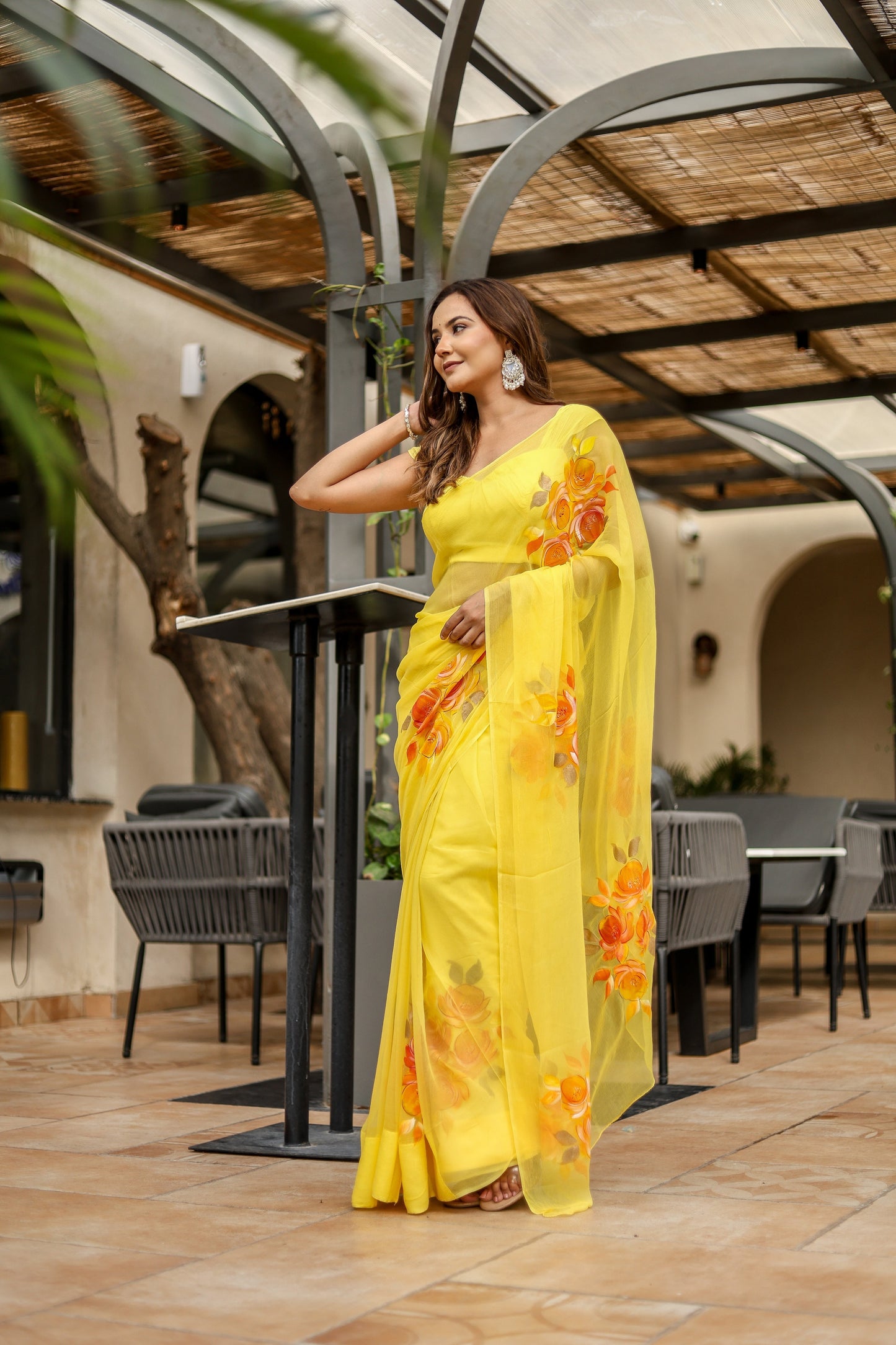 Model wearing a handpainted yellow chiffon saree with floral designs in a stylish outdoor setting