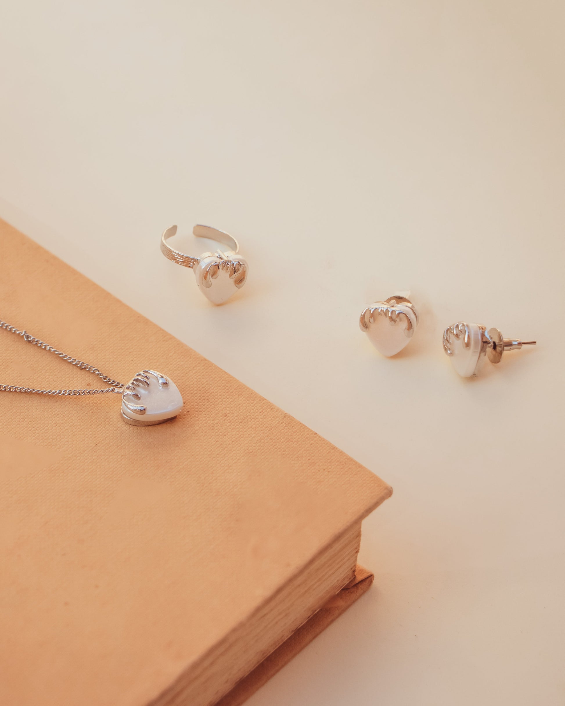 Stylera silver heart necklace with matching heart ring and stud earrings displayed on book