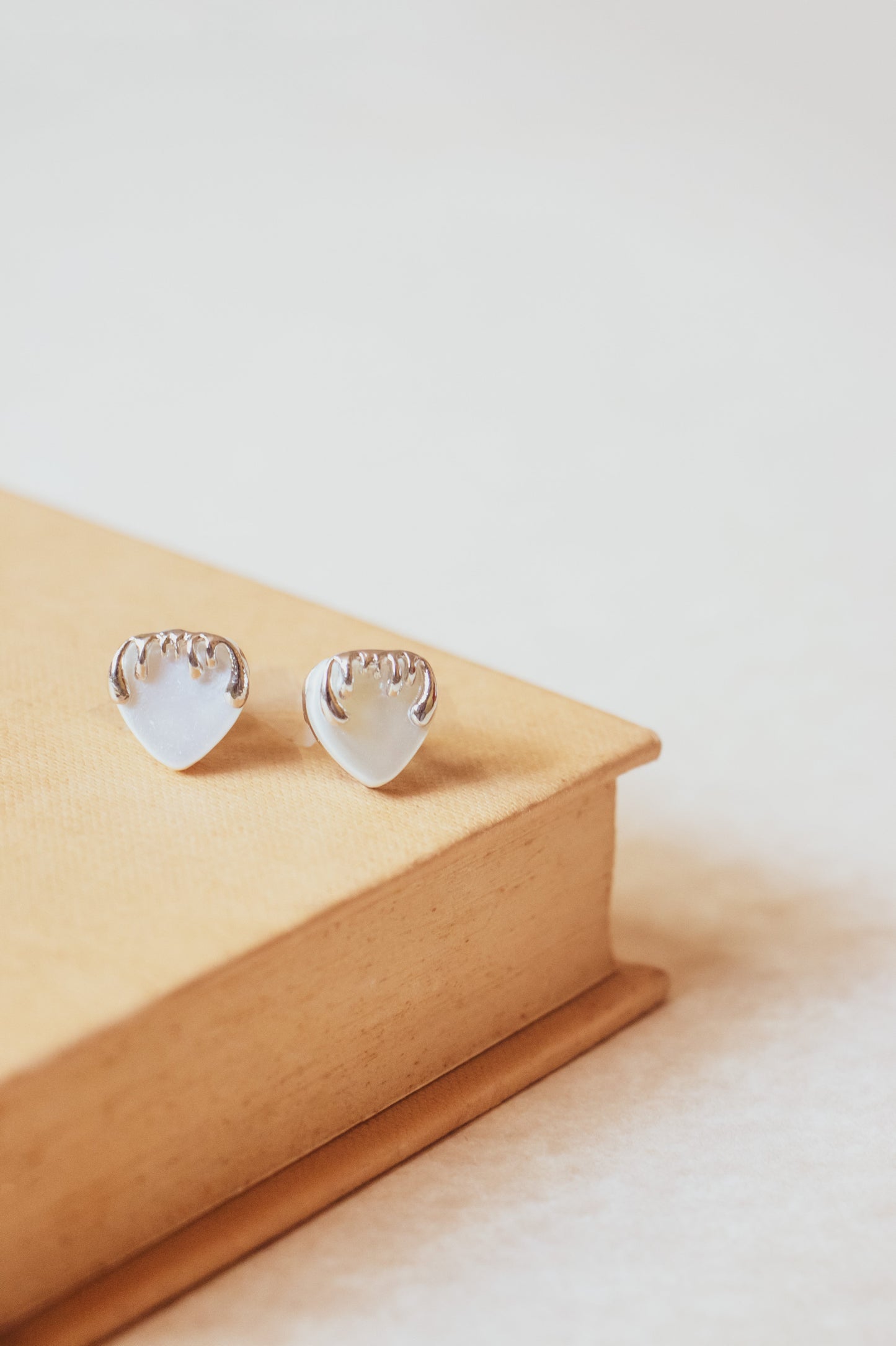 Stylera heart shaped silver stud earrings on beige book minimal background trendy silver accessories for women