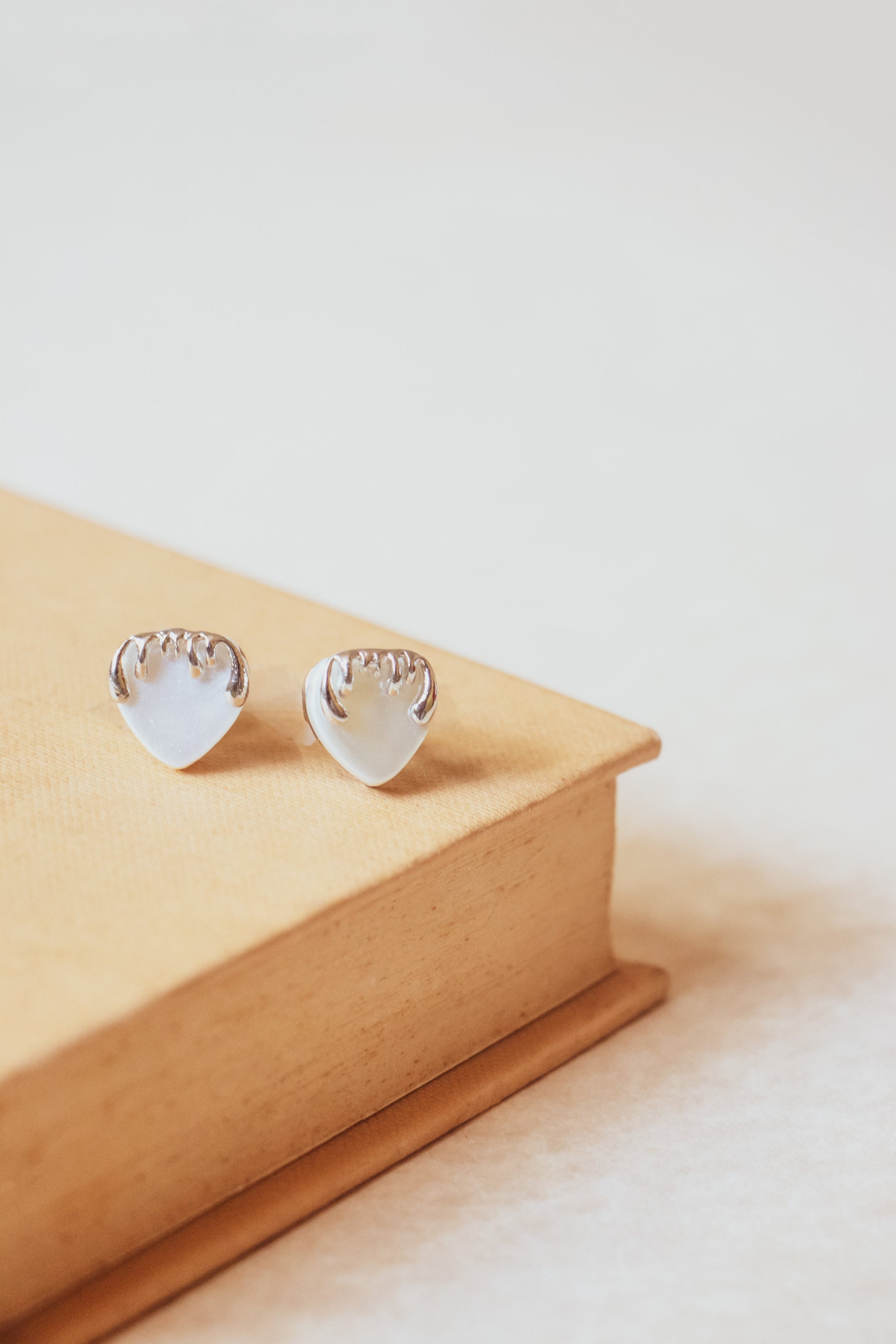 Stylera heart shaped silver stud earrings on beige book minimal background trendy silver accessories for women