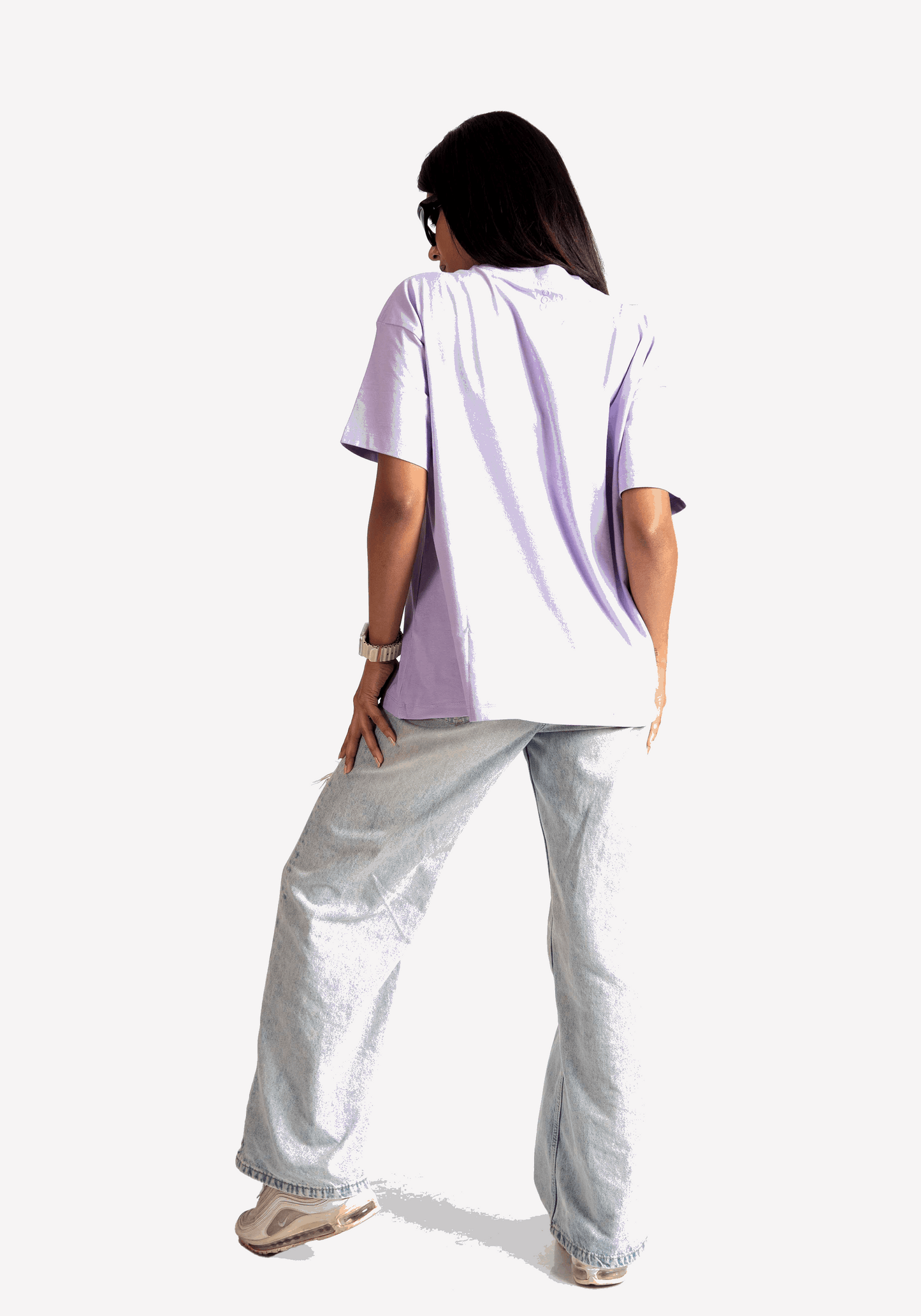 Back view of a woman wearing Stylera lavender oversized t-shirt with light wash jeans and sneakers