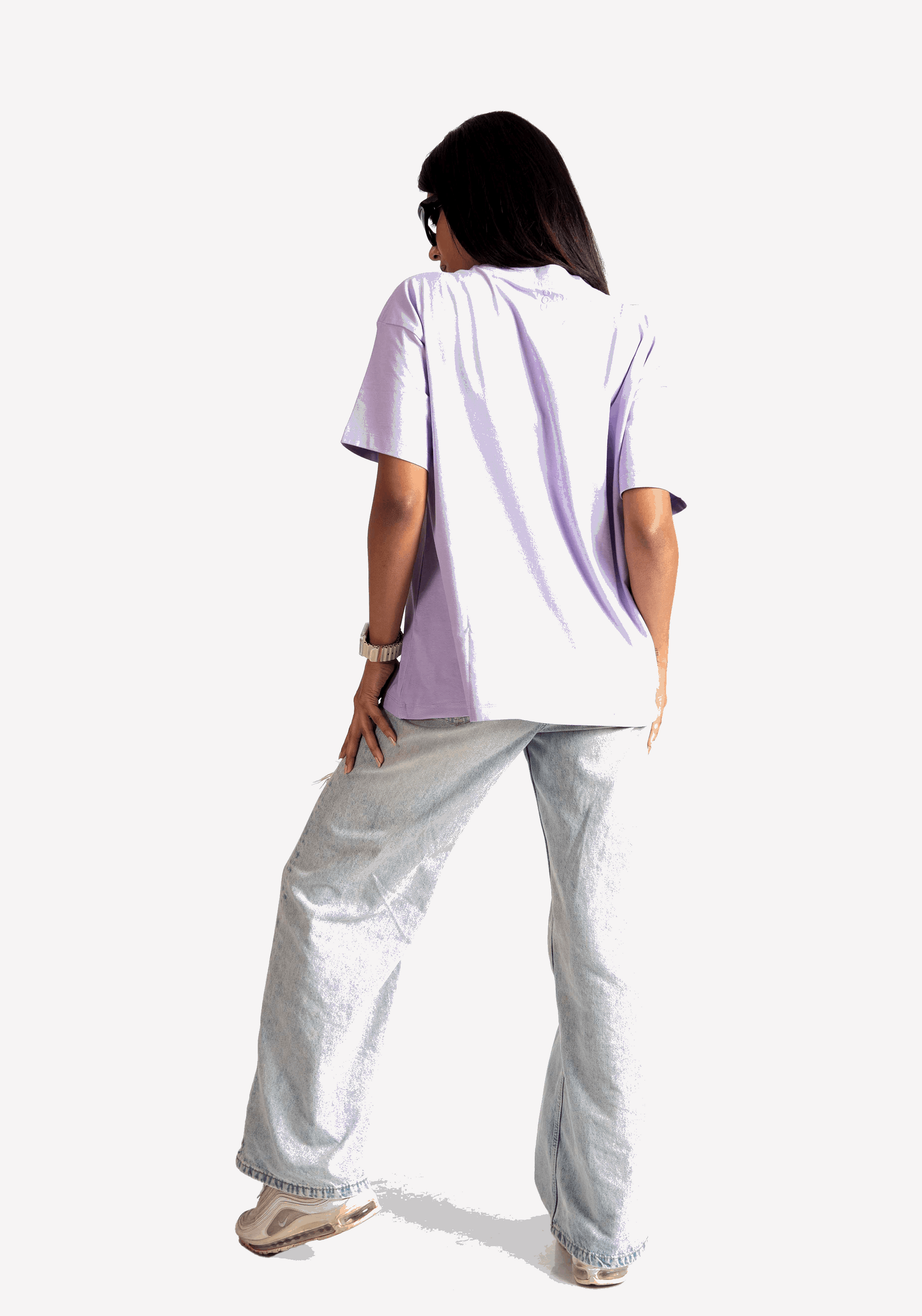 Back view of a woman wearing Stylera lavender oversized t-shirt with light wash jeans and sneakers