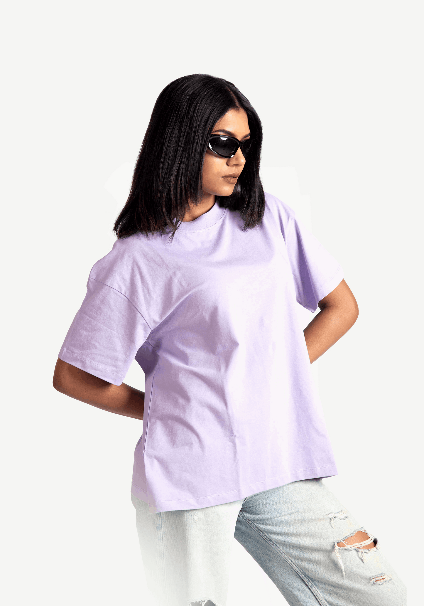 Woman wearing lavender oversized t-shirt from Stylera styled with ripped light jeans and black sunglasses