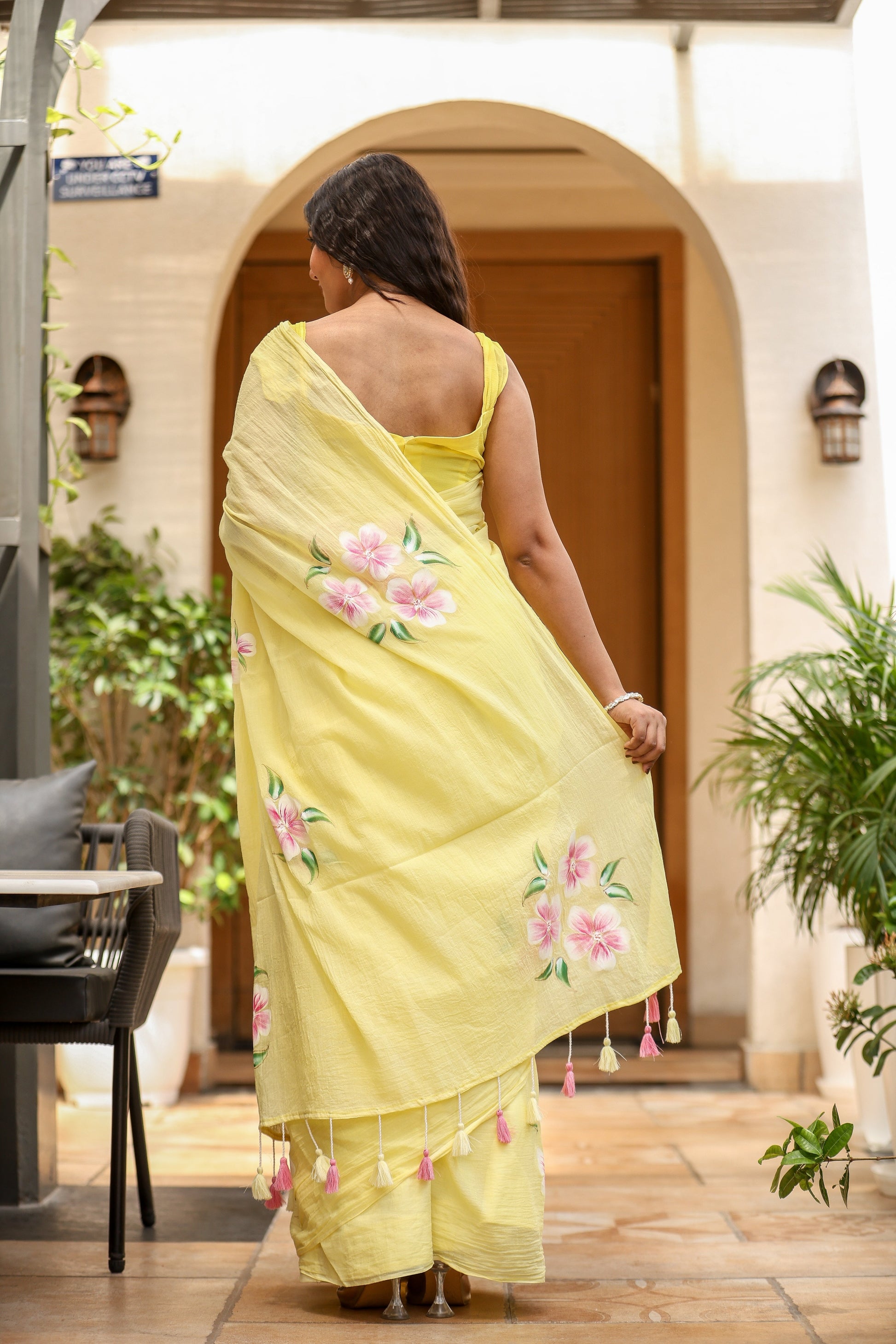 Women in a yellow lightweight party wear saree with floral embroidery and tassel details