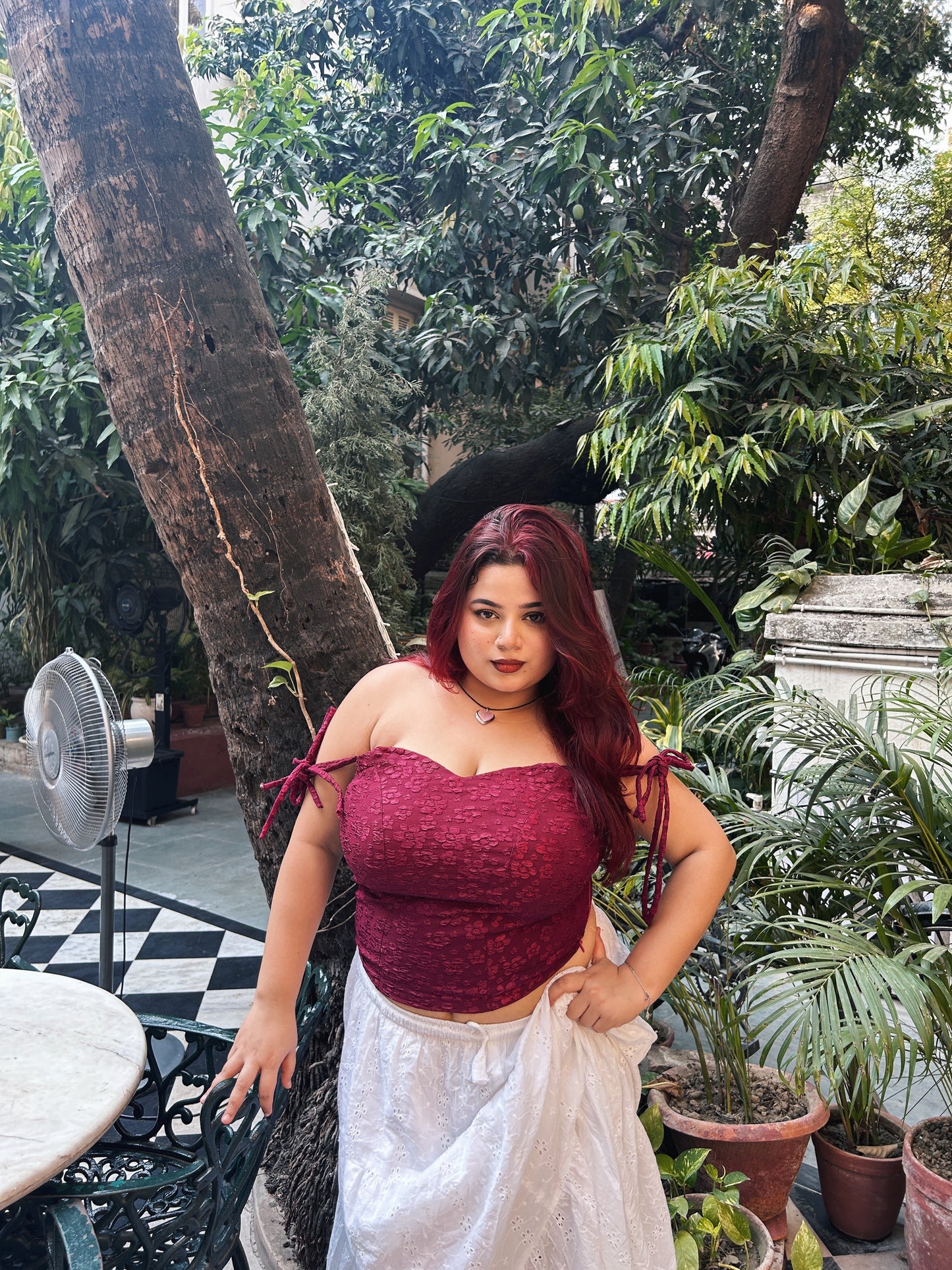 Model in a red lace corset top for women paired with white skirt in outdoor garden setting