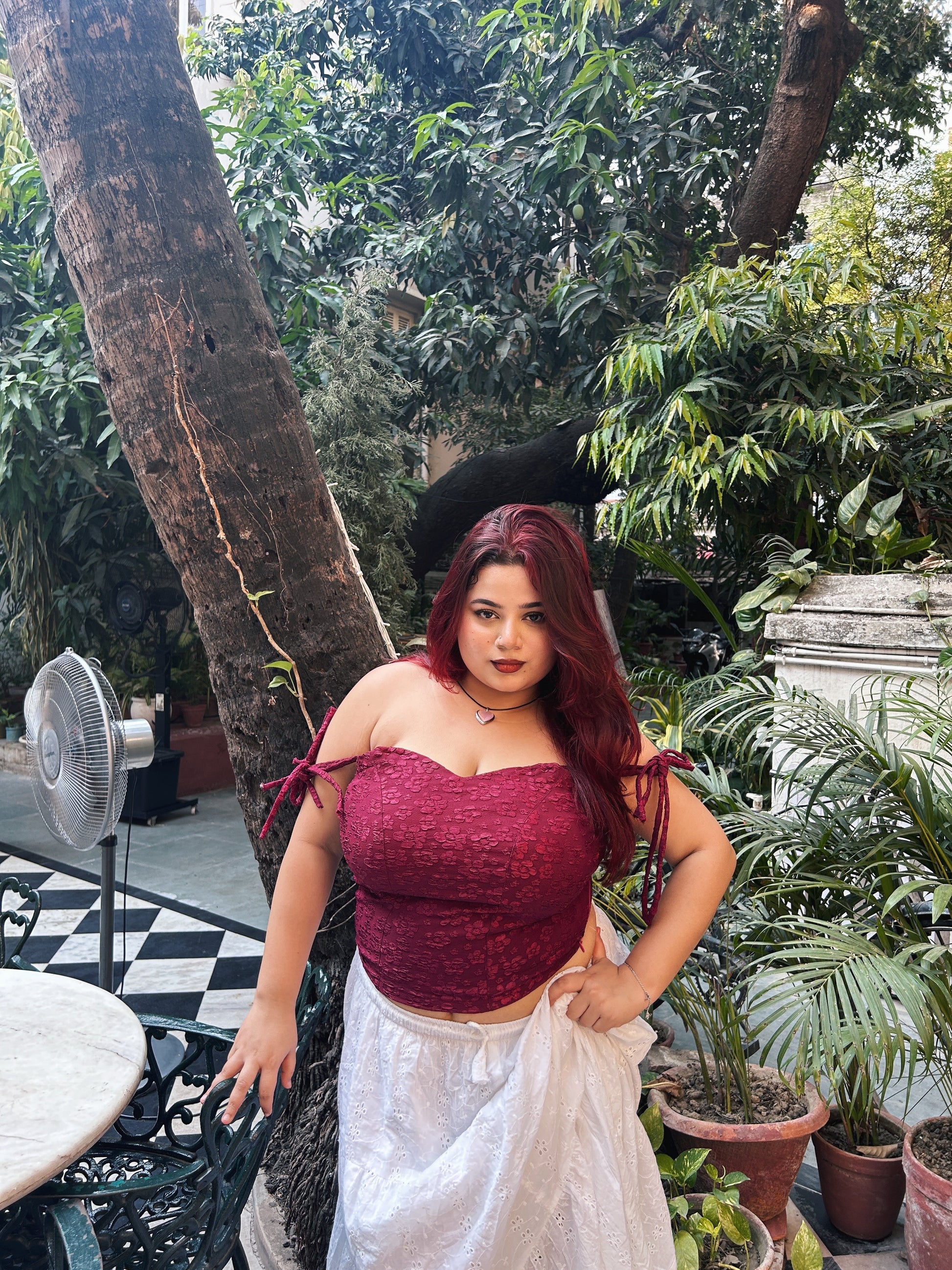 Model in a red lace corset top for women paired with white skirt in outdoor garden setting