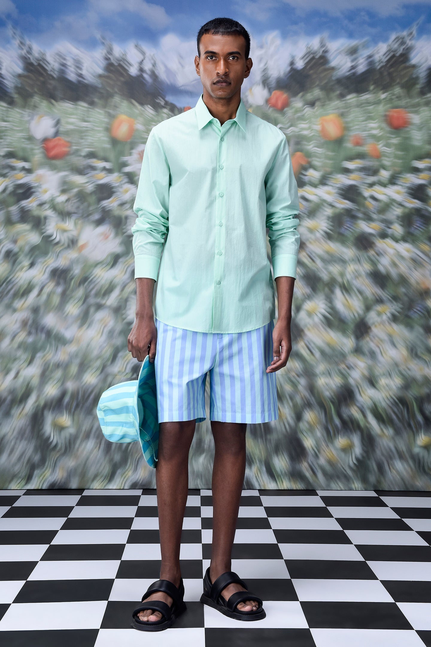 Male model wearing malmal regular fit formal shirt in mint green with striped blue shorts and hat on checkered floor