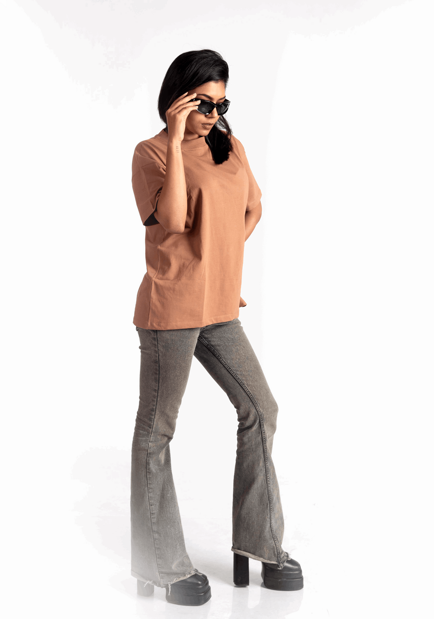 Woman wearing Stylera mocha brown oversized t-shirt paired with gray flared jeans and black platform shoes