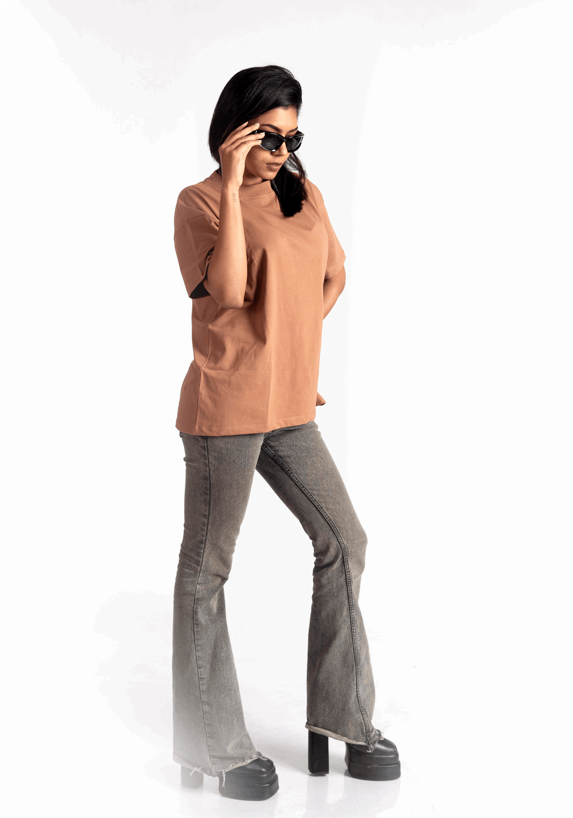 Woman wearing Stylera mocha brown oversized t-shirt paired with gray flared jeans and black platform shoes