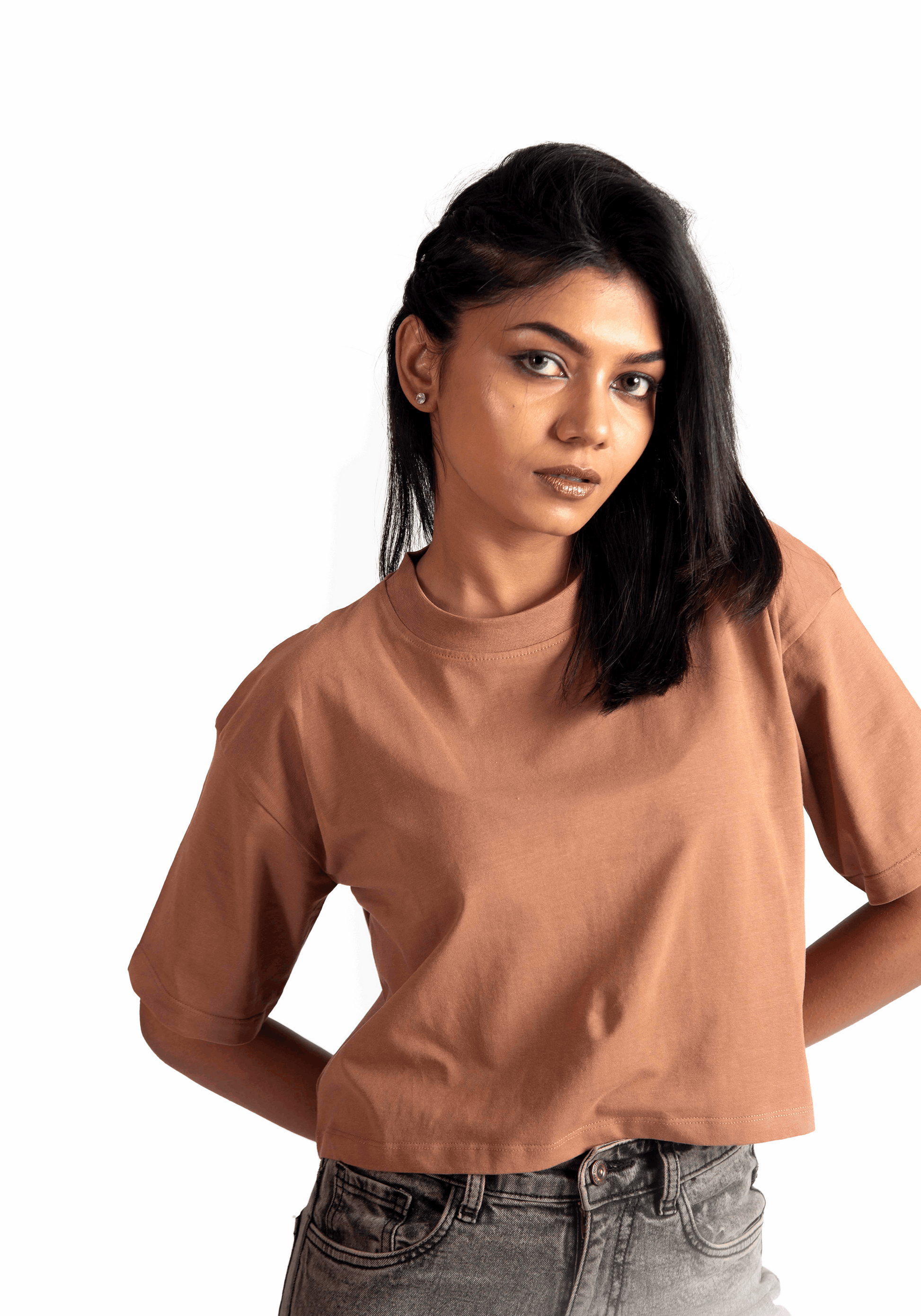 Woman wearing Stylera mocha oversized crop top paired with gray jeans against white background