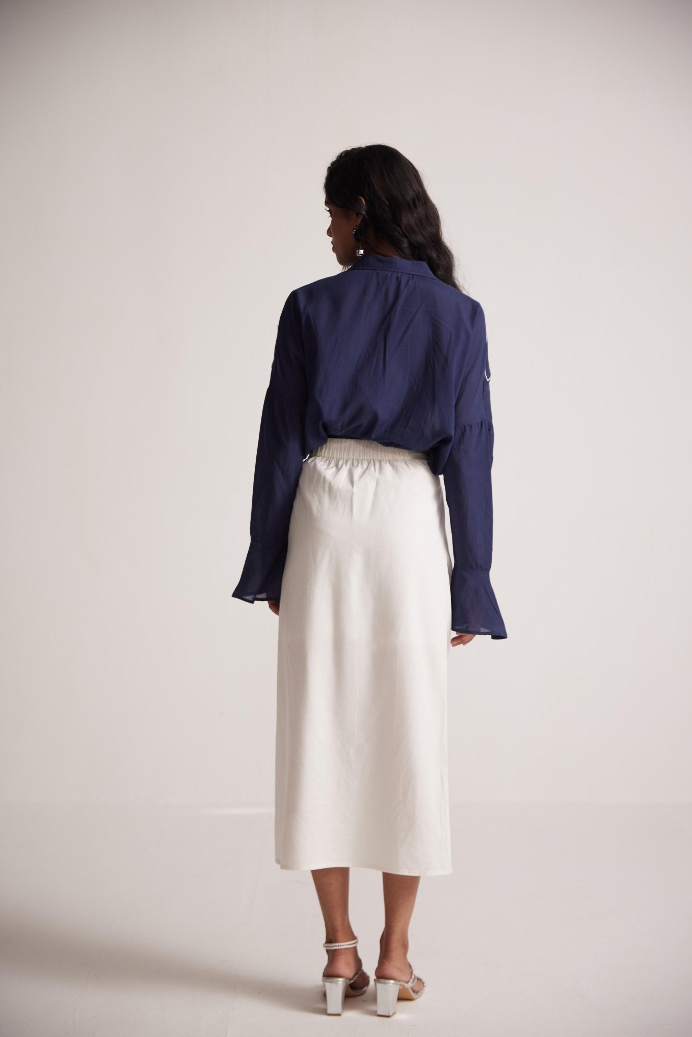 Back view of navy blue oversized cotton shirt by Stylera worn with white midi skirt and heels