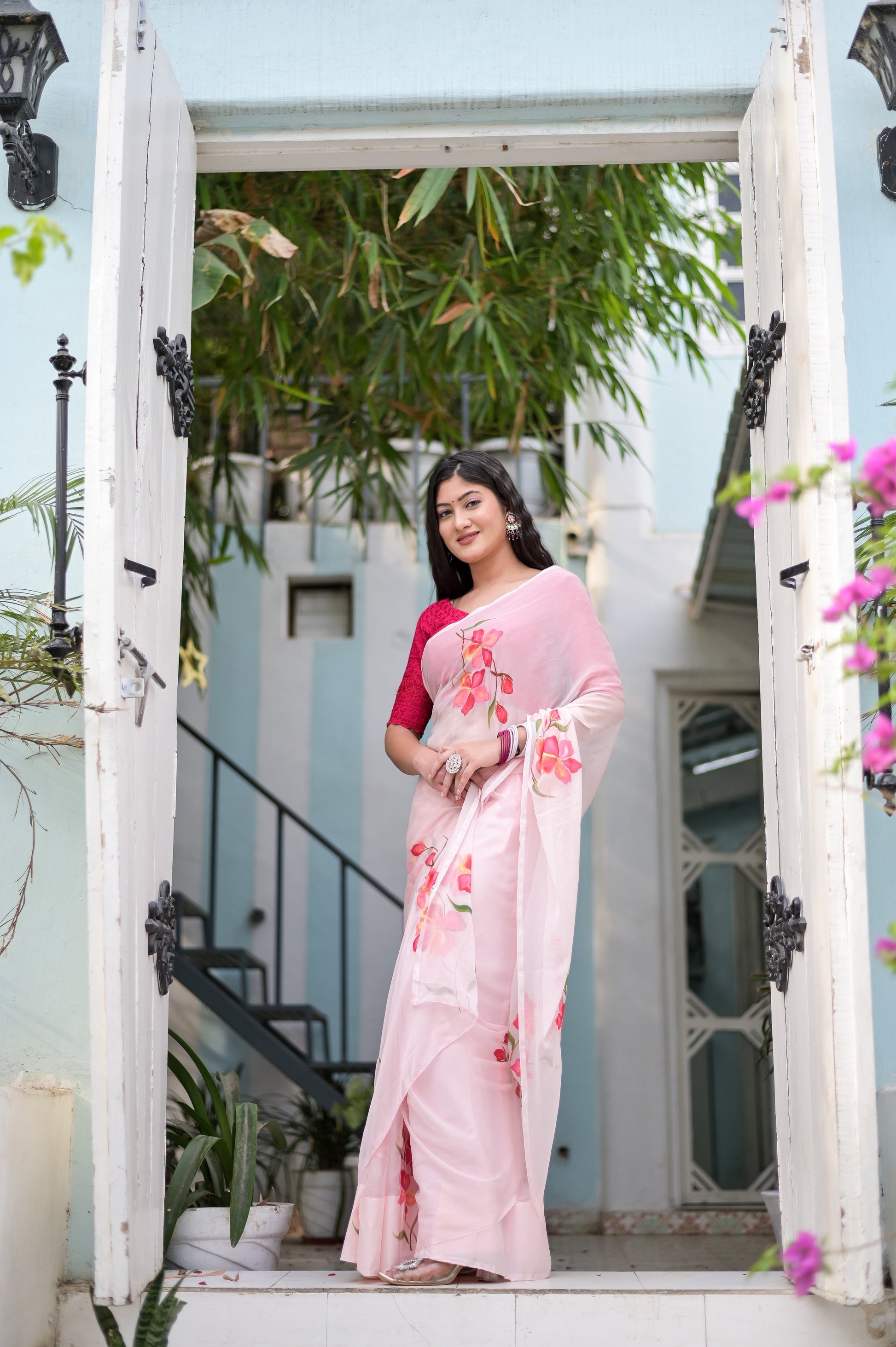 Elegant pink saree for women with floral embroidery, worn by a model at a picturesque entrance