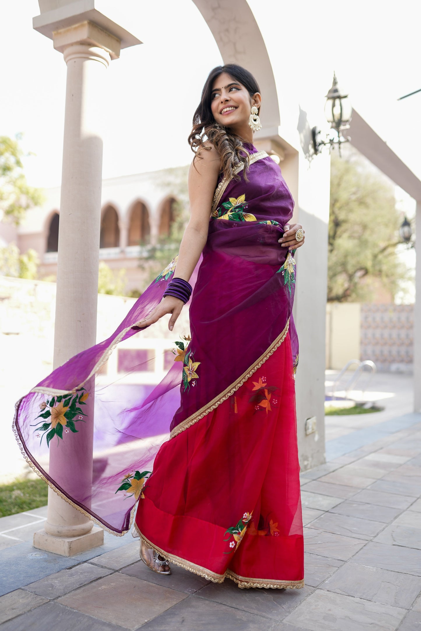 Stunning red and purple saree with handwork, worn elegantly by a model in a scenic outdoor setting