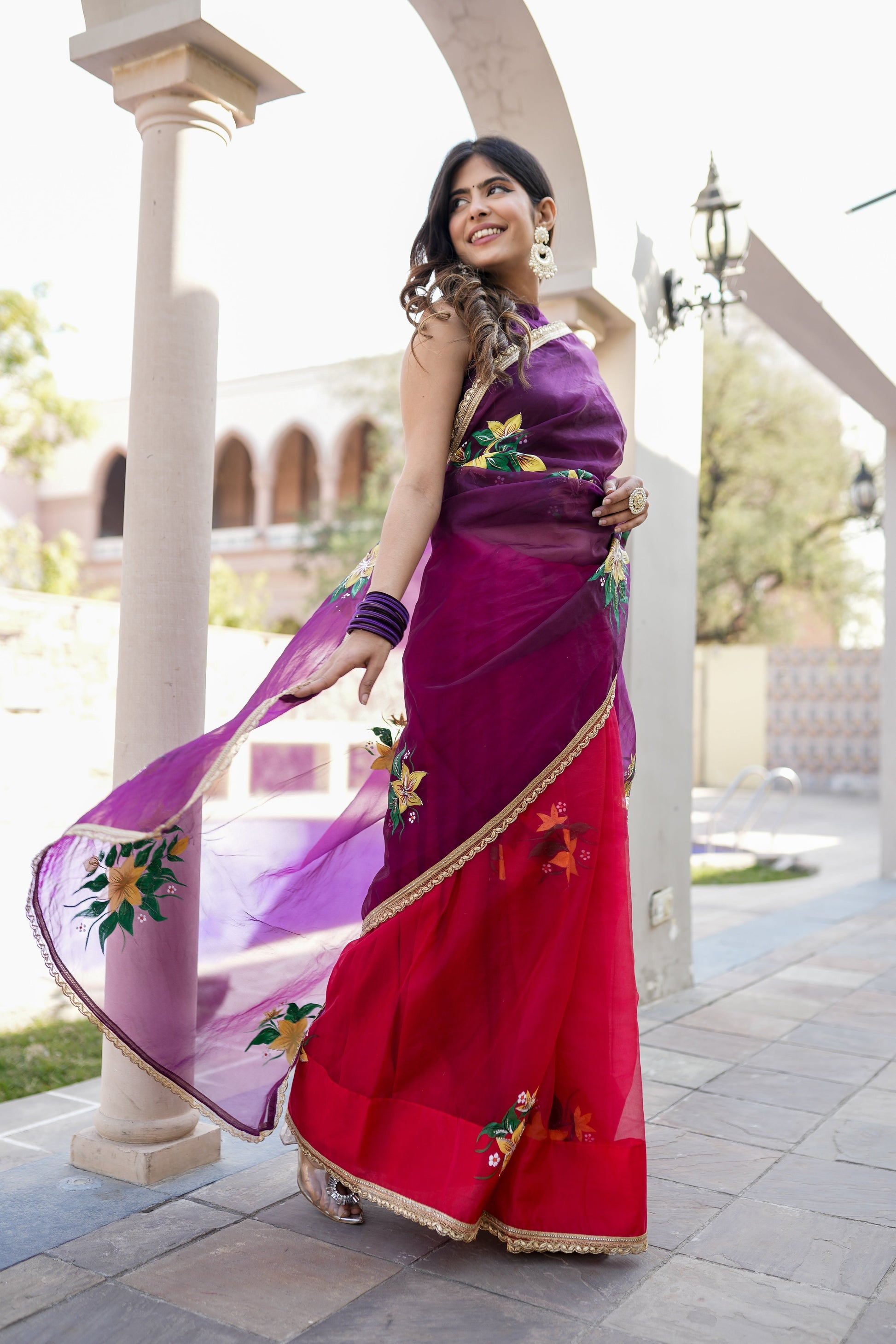 Stunning red and purple saree with handwork, worn elegantly by a model in a scenic outdoor setting