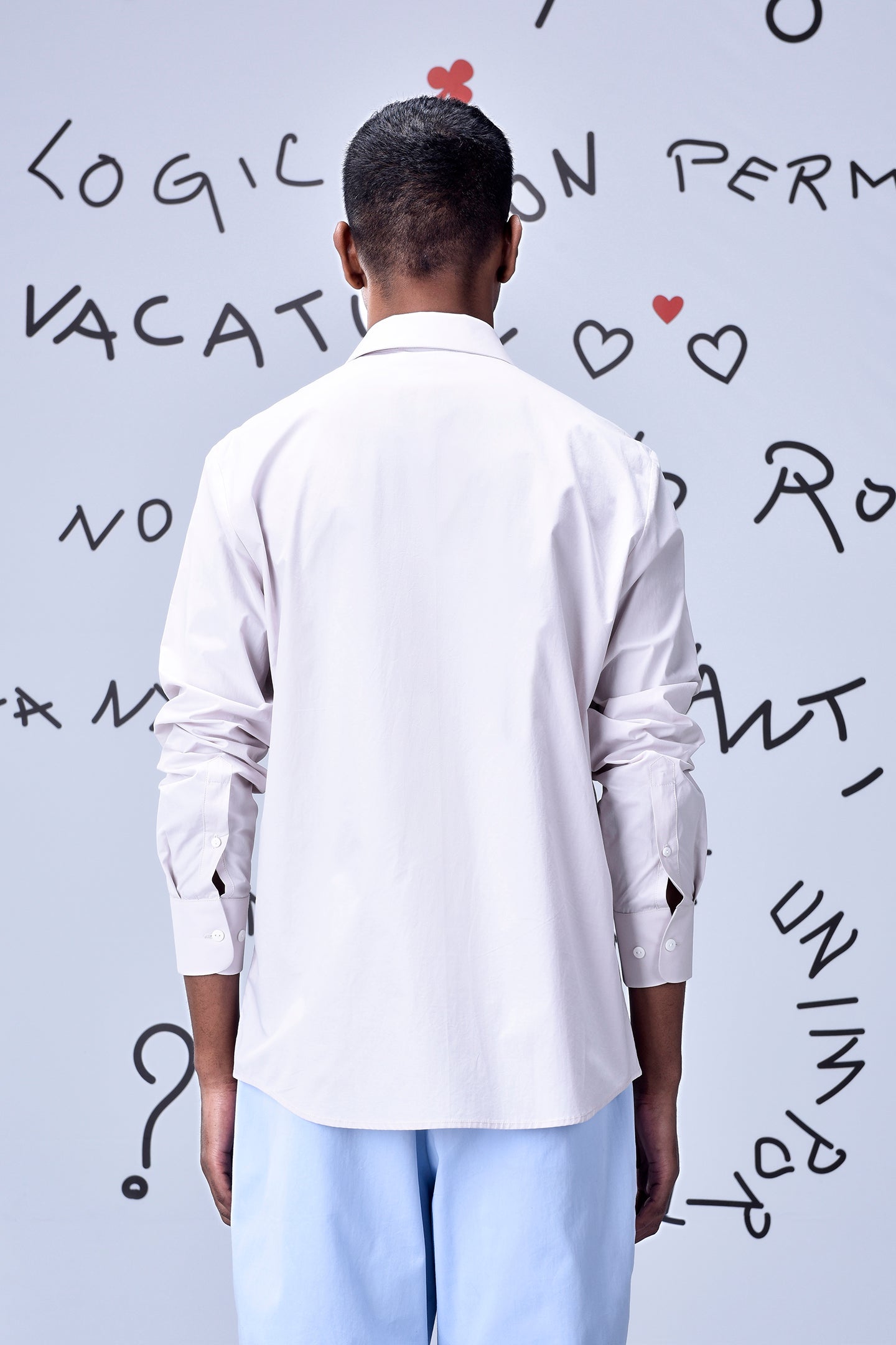 Back view of model wearing Stylera white regular fit men's shirt cotton with light blue trousers and doodle backdrop