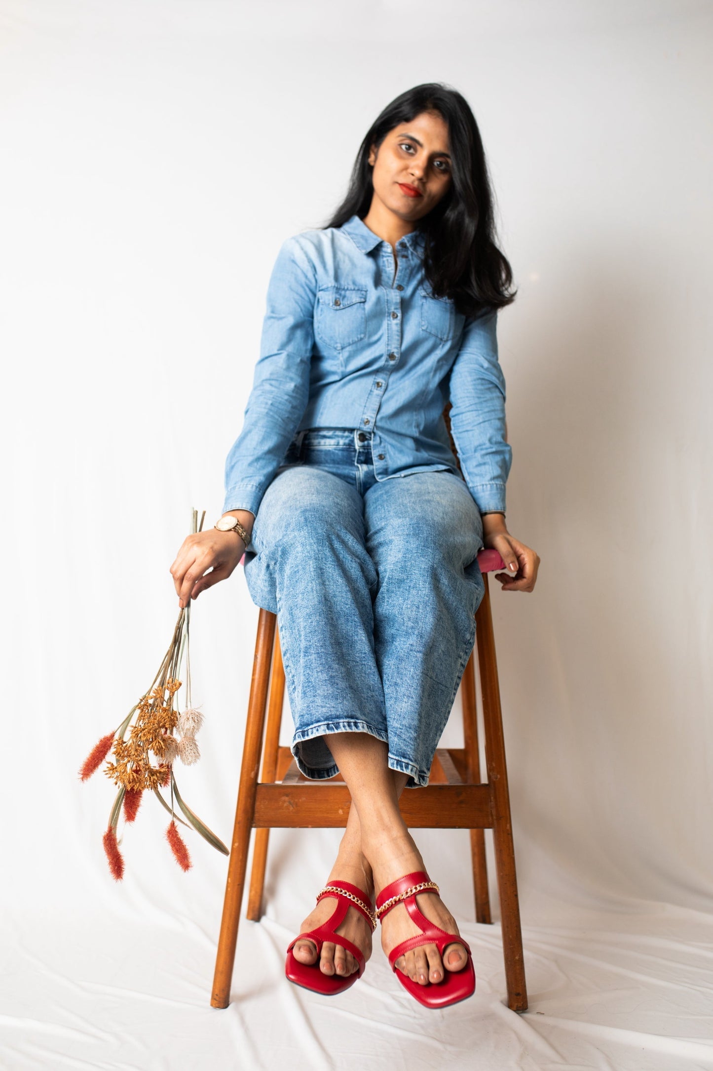 Stylera stylish red flat sandals worn by woman sitting on wooden stool with denim outfit