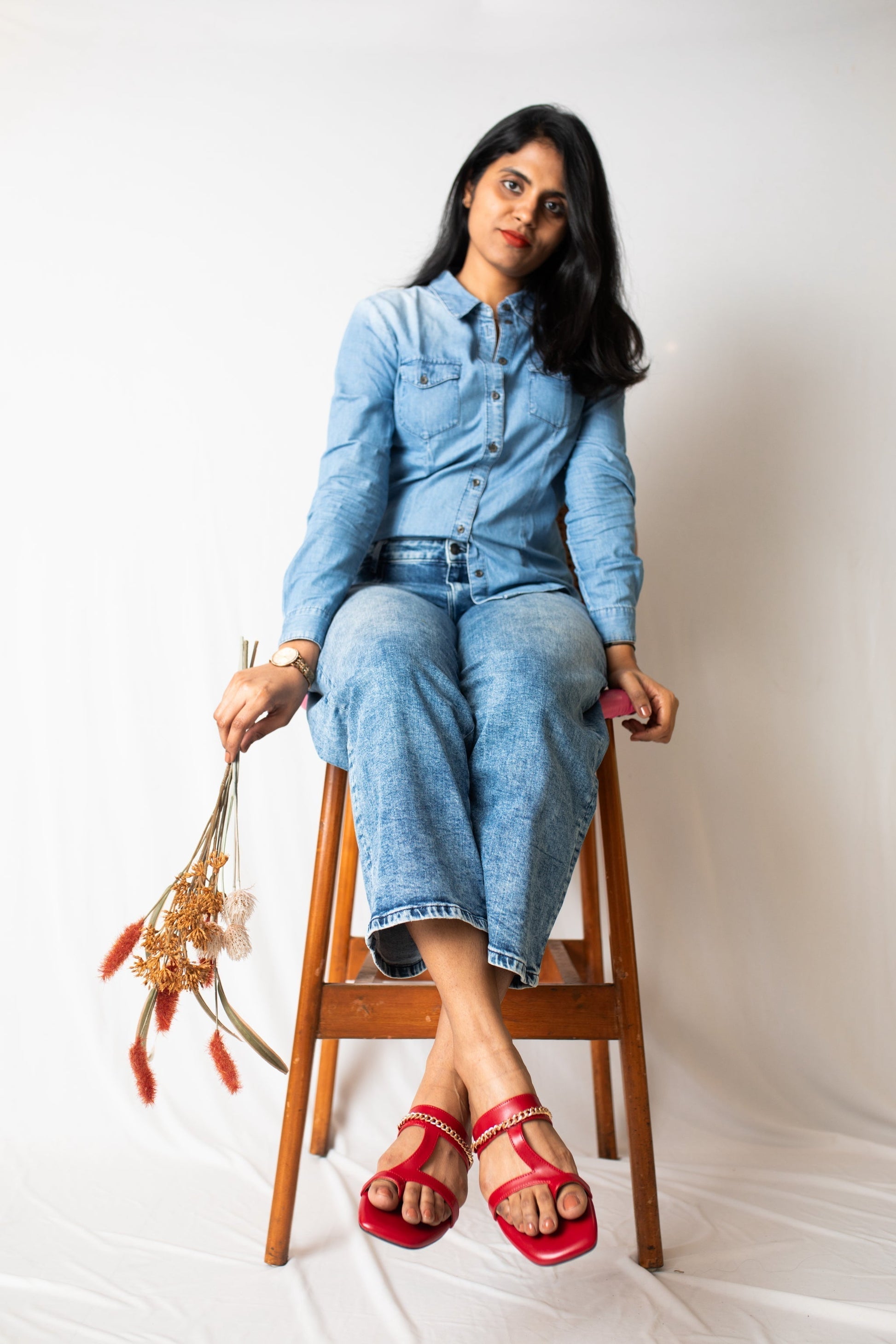 Stylera stylish red flat sandals worn by woman sitting on wooden stool with denim outfit