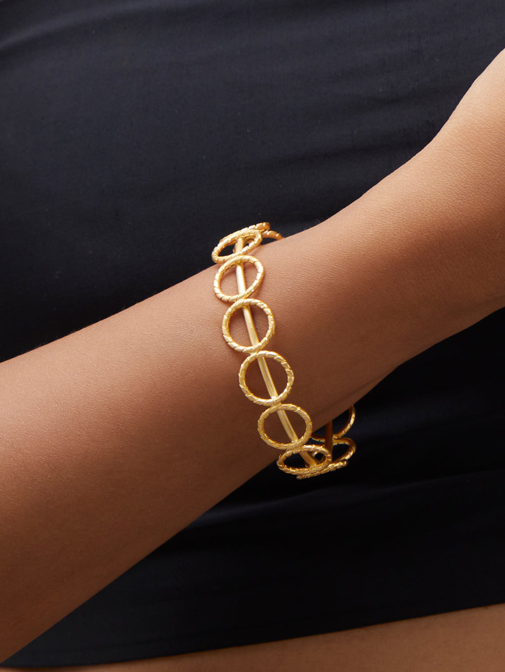 Stylera trendy gold accessory bracelet of linked textured gold circles worn on wrist with black top