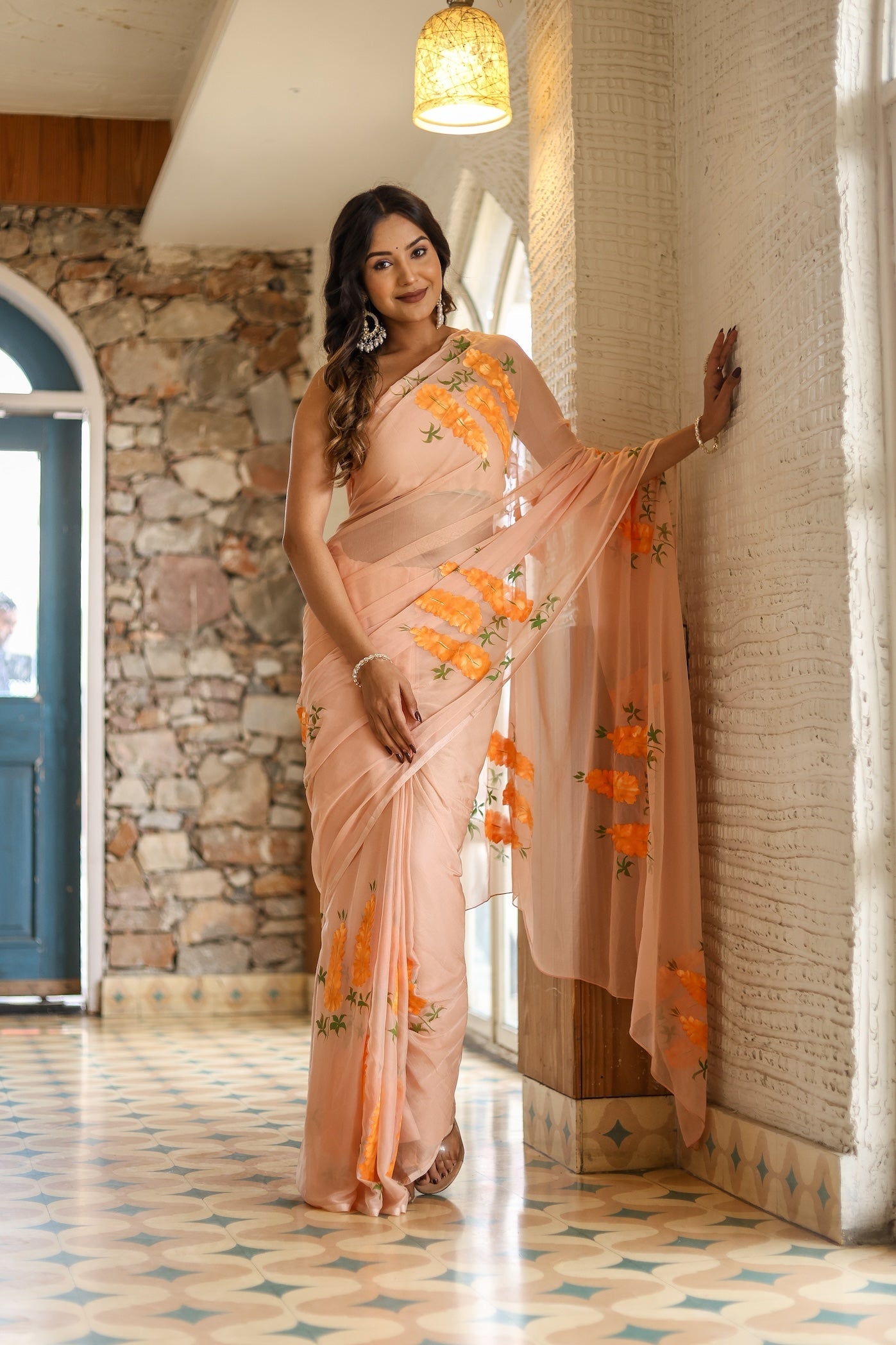 Elegant woman in a trendy peach saree with floral design posing in a stylish indoor setting
