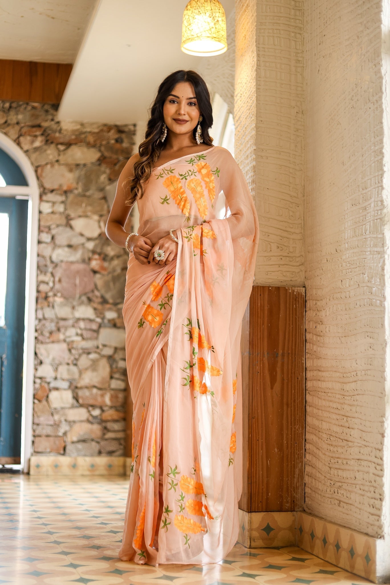 Trendy peach saree with floral design, elegantly draped on a model in a scenic indoor setting