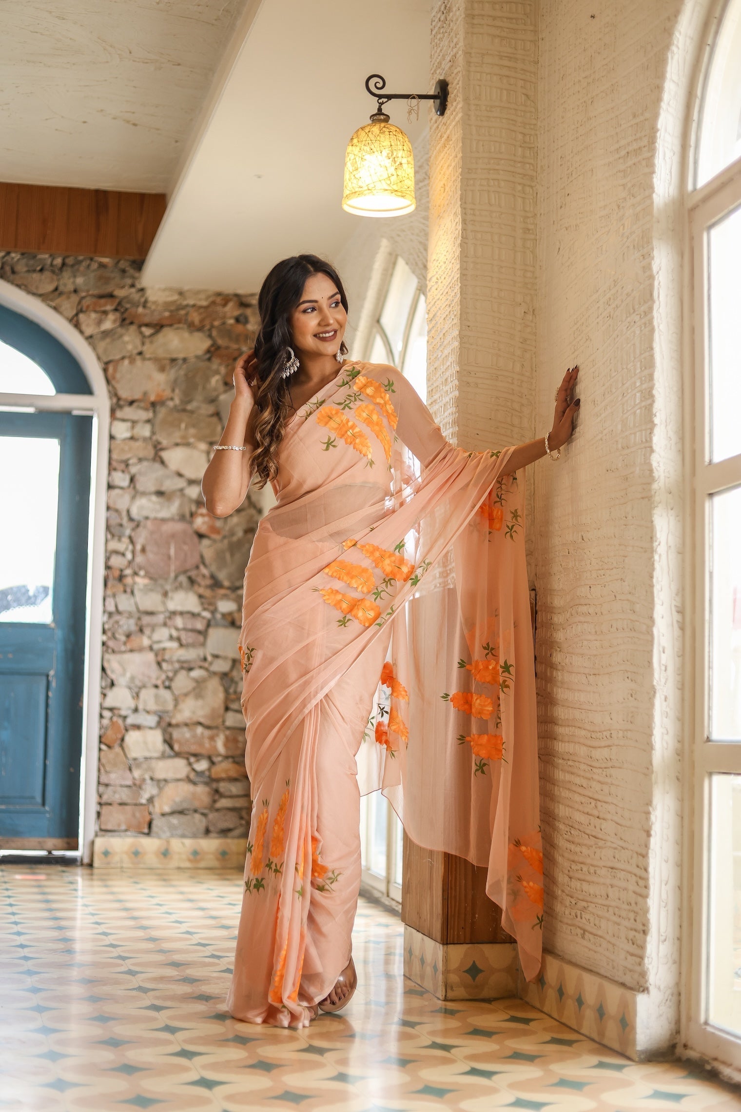 Model wearing a trendy peach saree with floral design, showcasing elegance in a stylish indoor setting