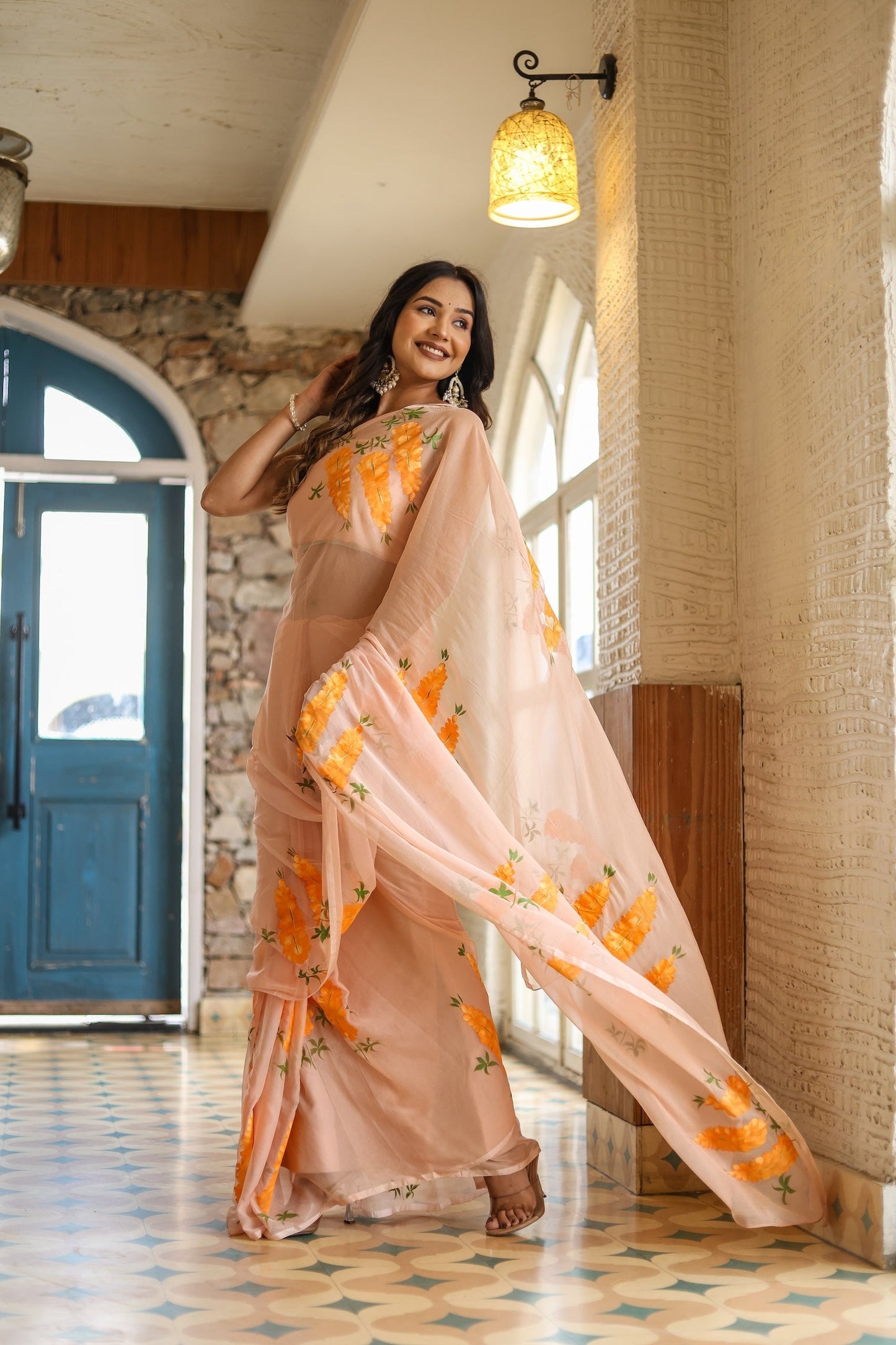 Model in a trendy peach saree with floral design showcasing elegance and style in a bright interior