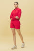 Model wearing Stylera trendy red matching shorts and shirt set with collared long sleeve shirt and white sneakers