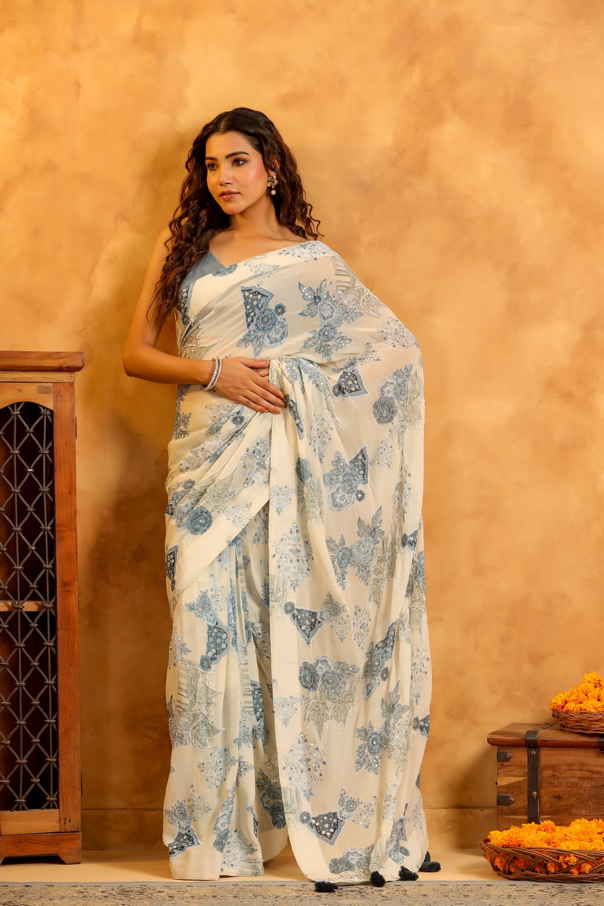 Stylera model wearing a trendy saree with blouse set white saree with blue floral and butterfly print against warm tan backdrop