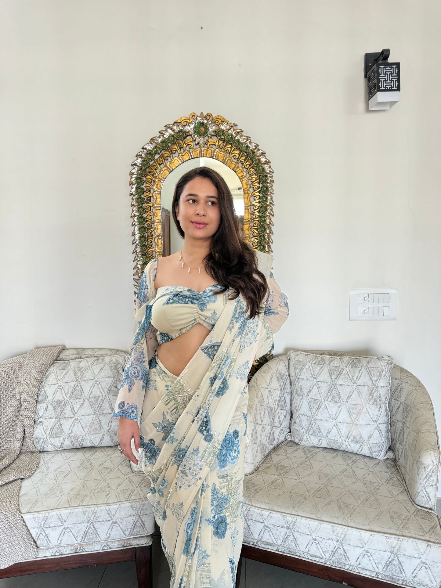 Woman modeling trendy saree with blouse set cream and blue floral print in living room with decorative mirror