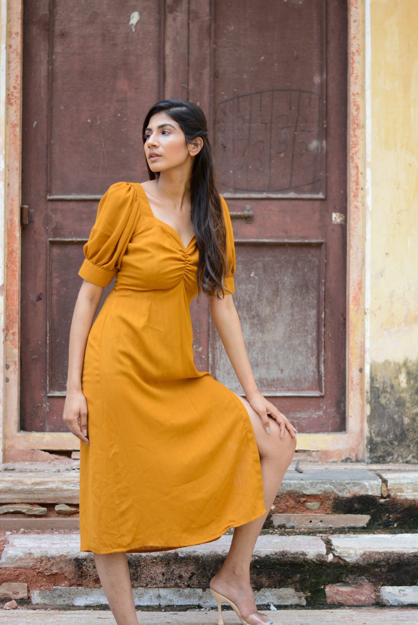 Trendy yellow slit midi dress featured on a model posing by a vintage door