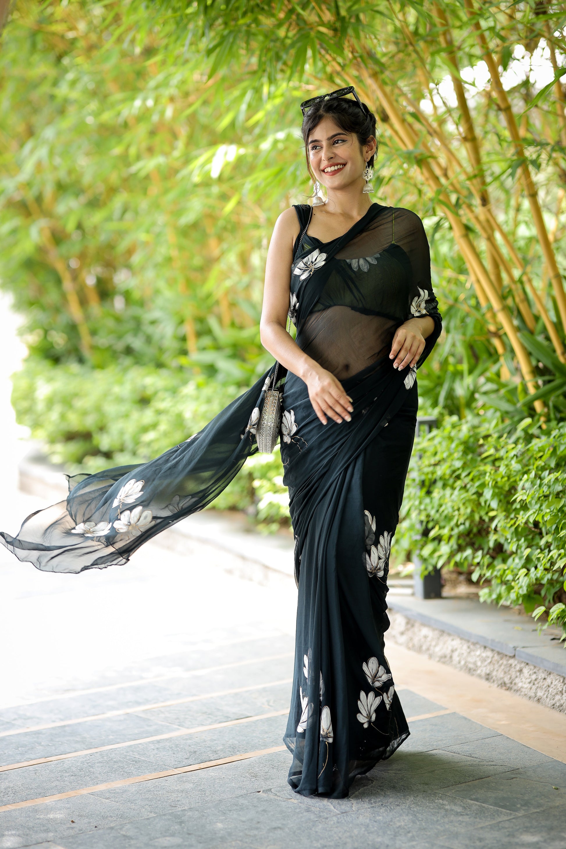 Elegant woman in a unique black saree for party wear, walking gracefully in a lush garden