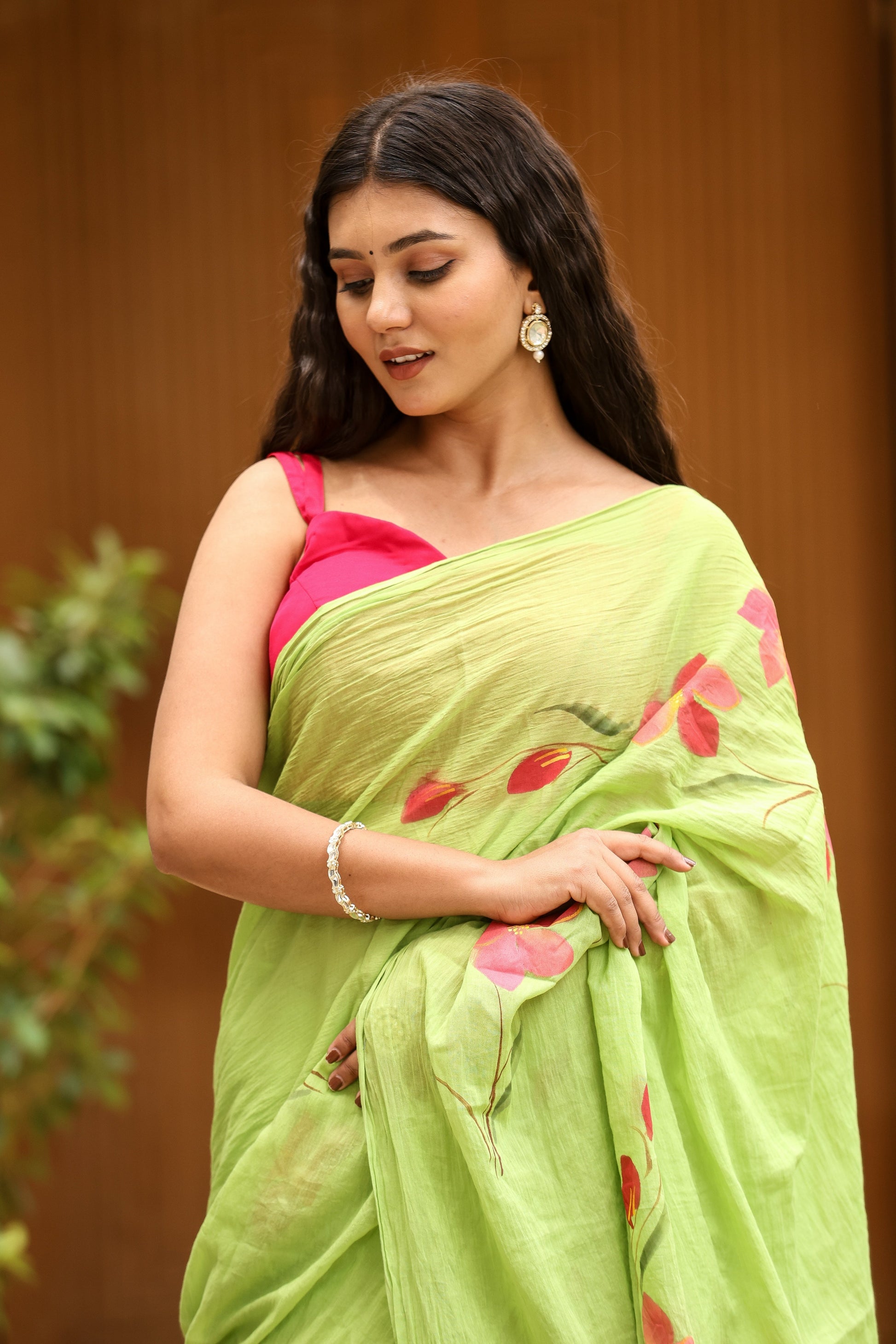 Elegant woman wearing a unique designer malmal saree in green with floral patterns, styled with a pink blouse.